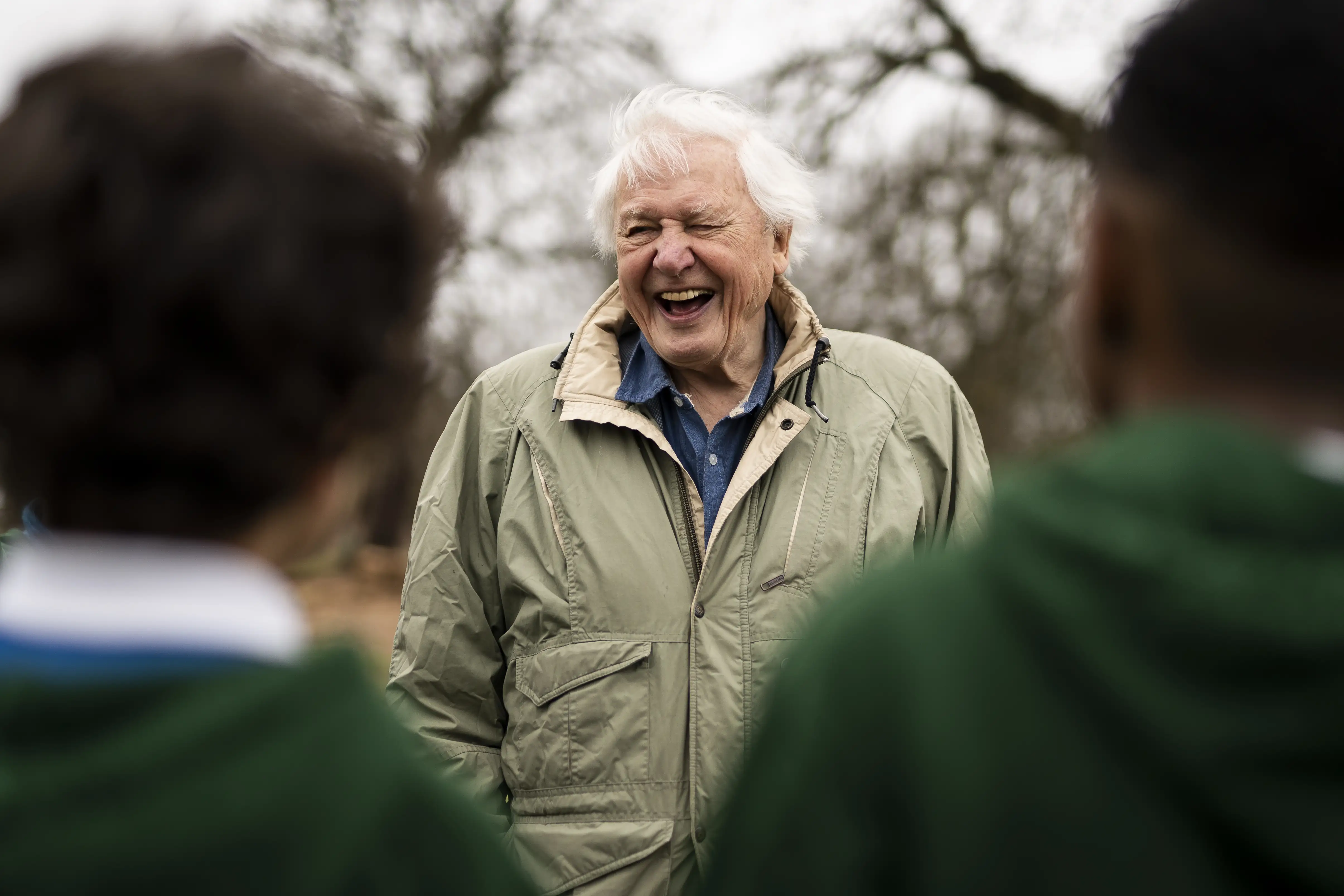 Sir David Attenborough laughing with school children during a tree planting in 2023