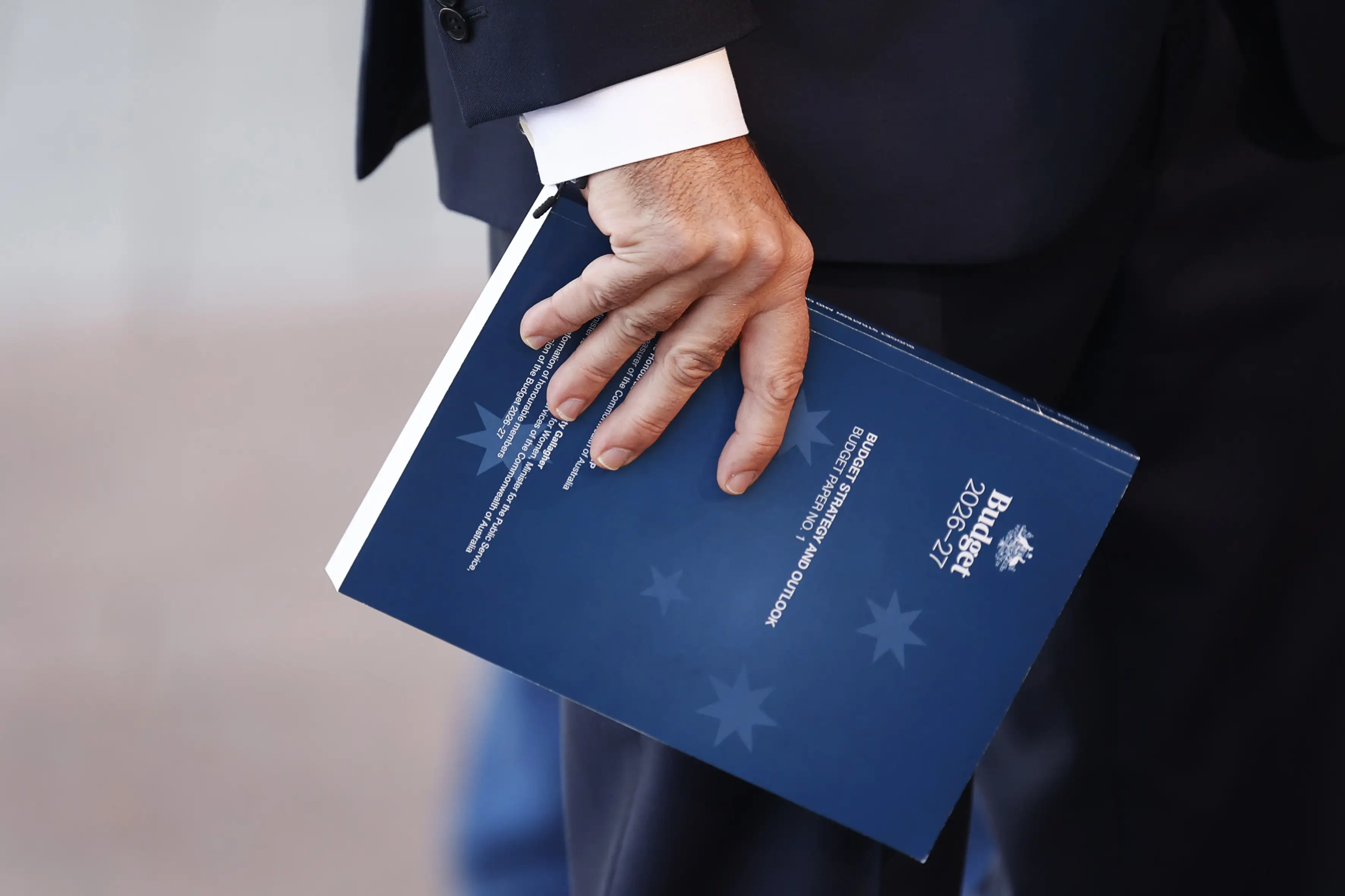 Treasurer Jim Chalmers holds a copy of the 2026 budget while speaking with the media at Australian Parliament House
