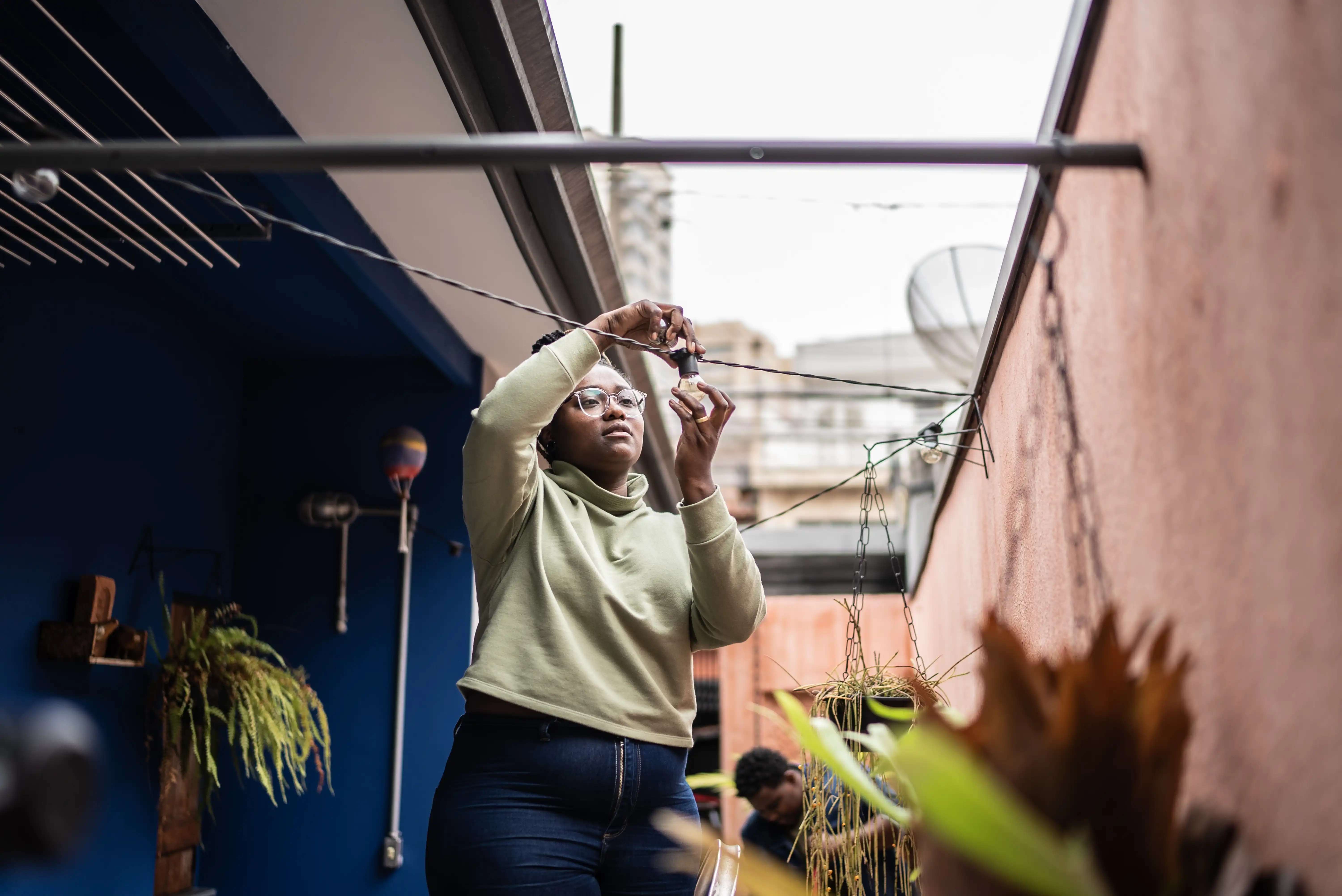 A woman fixes a hanging light in her backyard