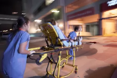 Two nurses pushing a person on a trolley into a hospital at night