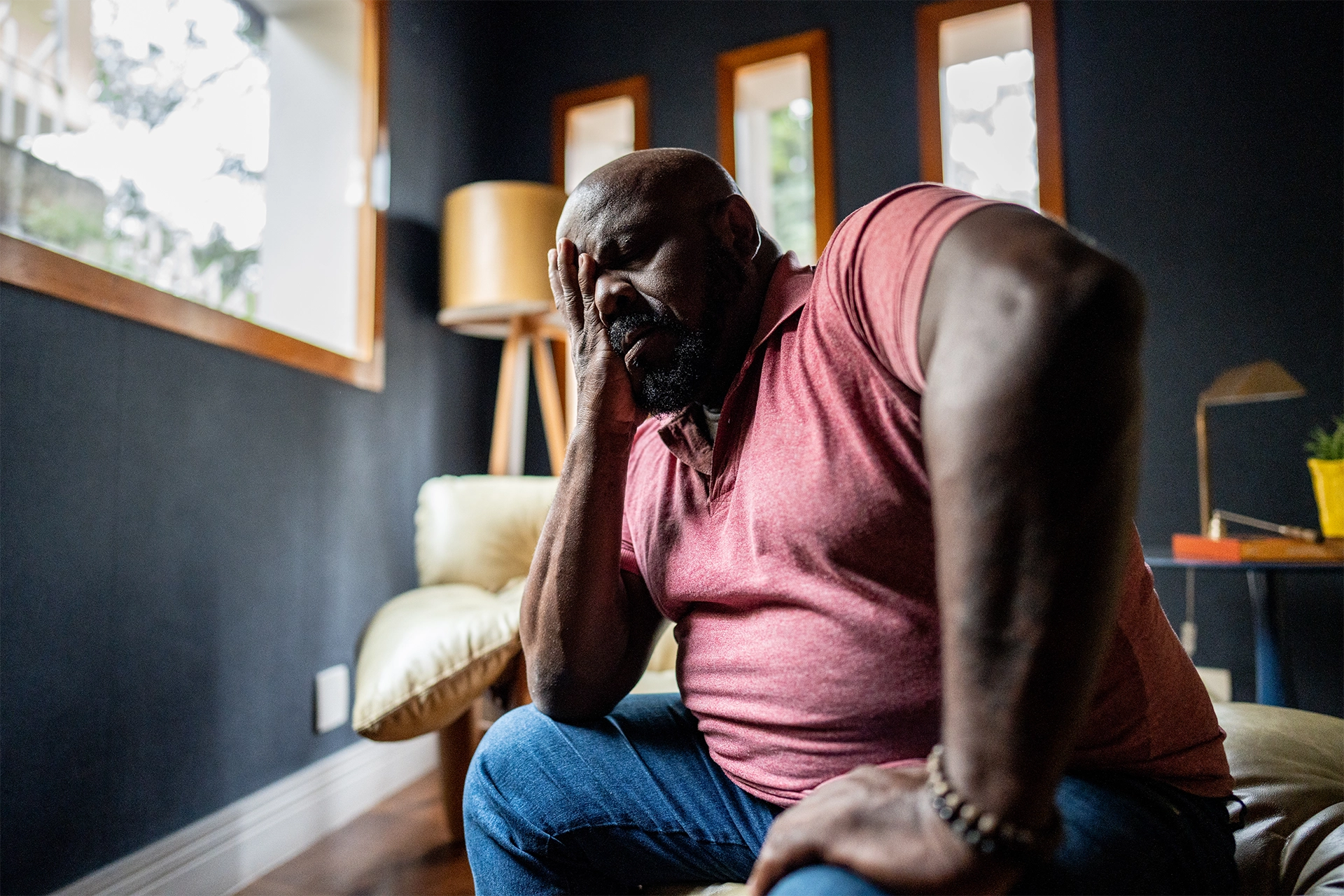 Large man sitting on a bed resting his head on his hand