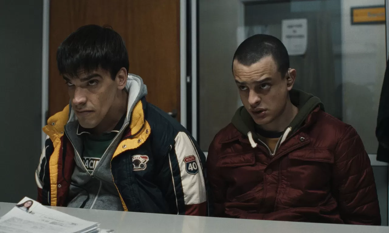 A movie still of two men sitting at a table looking worried