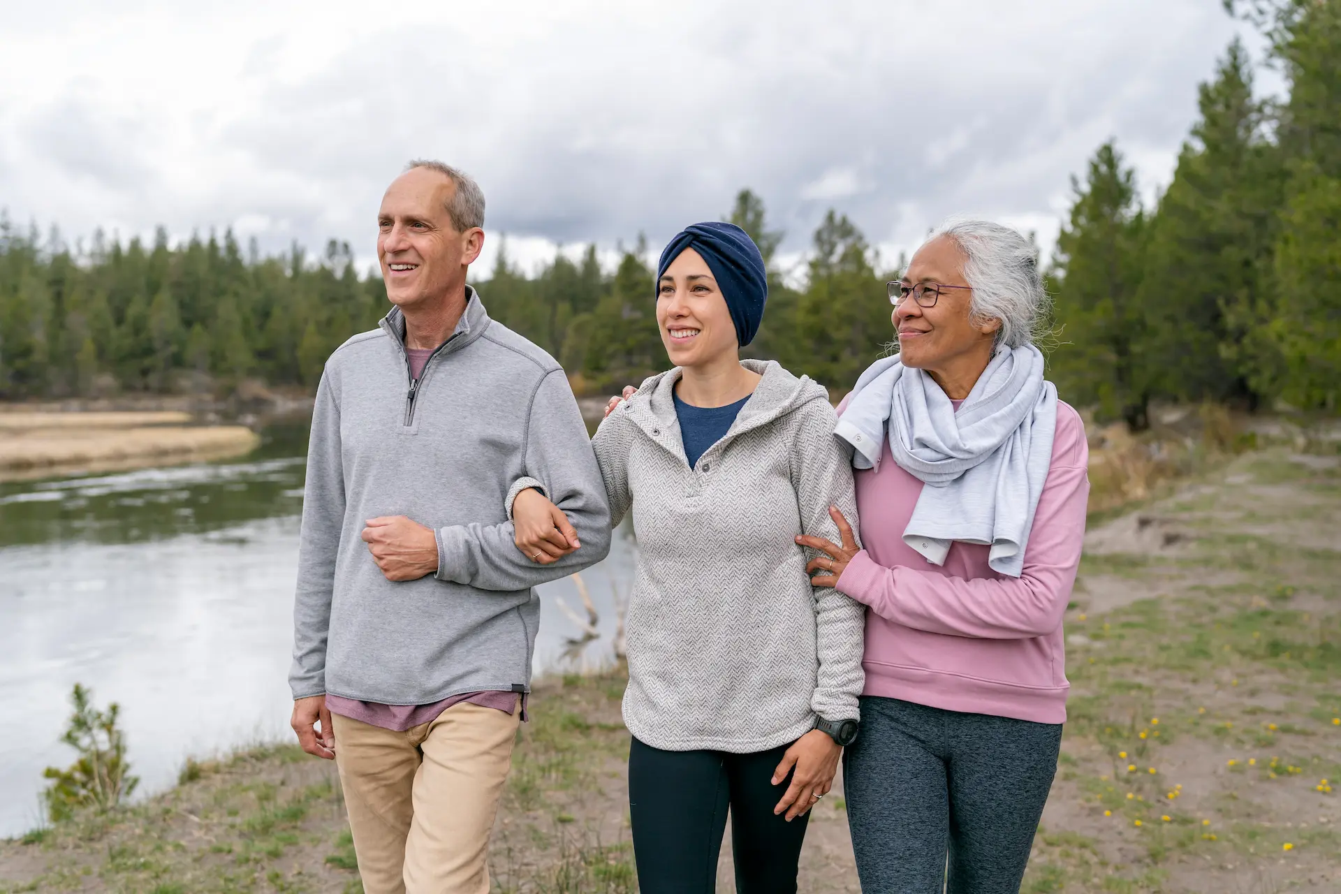 Three people walking arm in arm beside a river