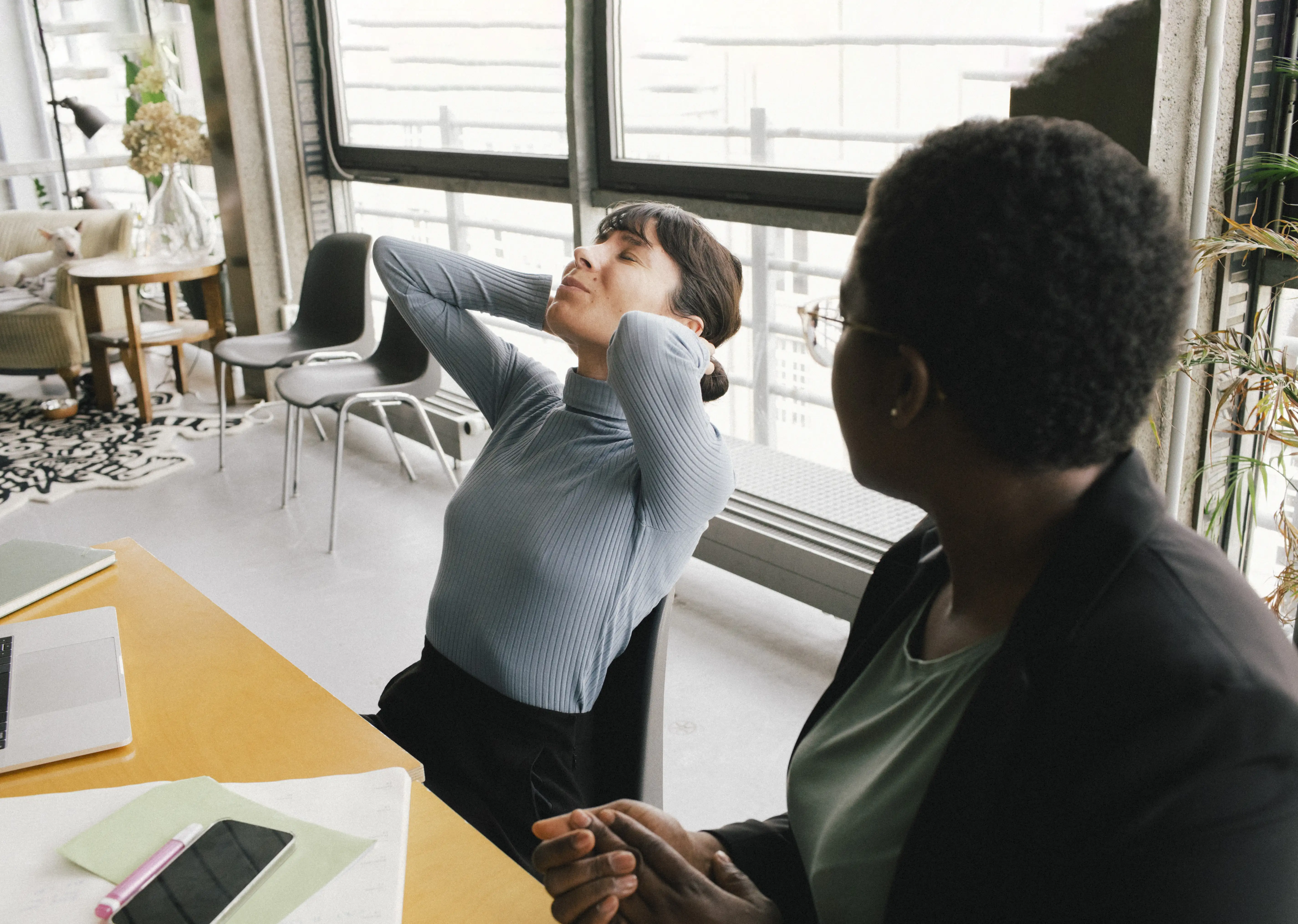 A woman stretching back in pain next to her colleague