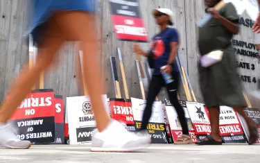 Strike signs line the sidewalk as members of the Writers Guild of America and the Screen Actors Guild walk the picket line