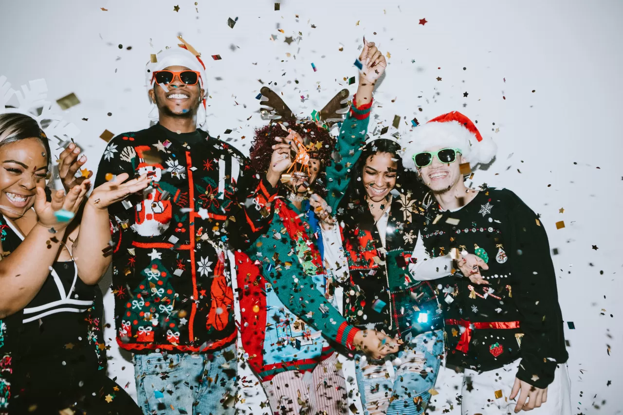 A group of teenagers various Christmas accessories and ugly sweaters throwing glitter