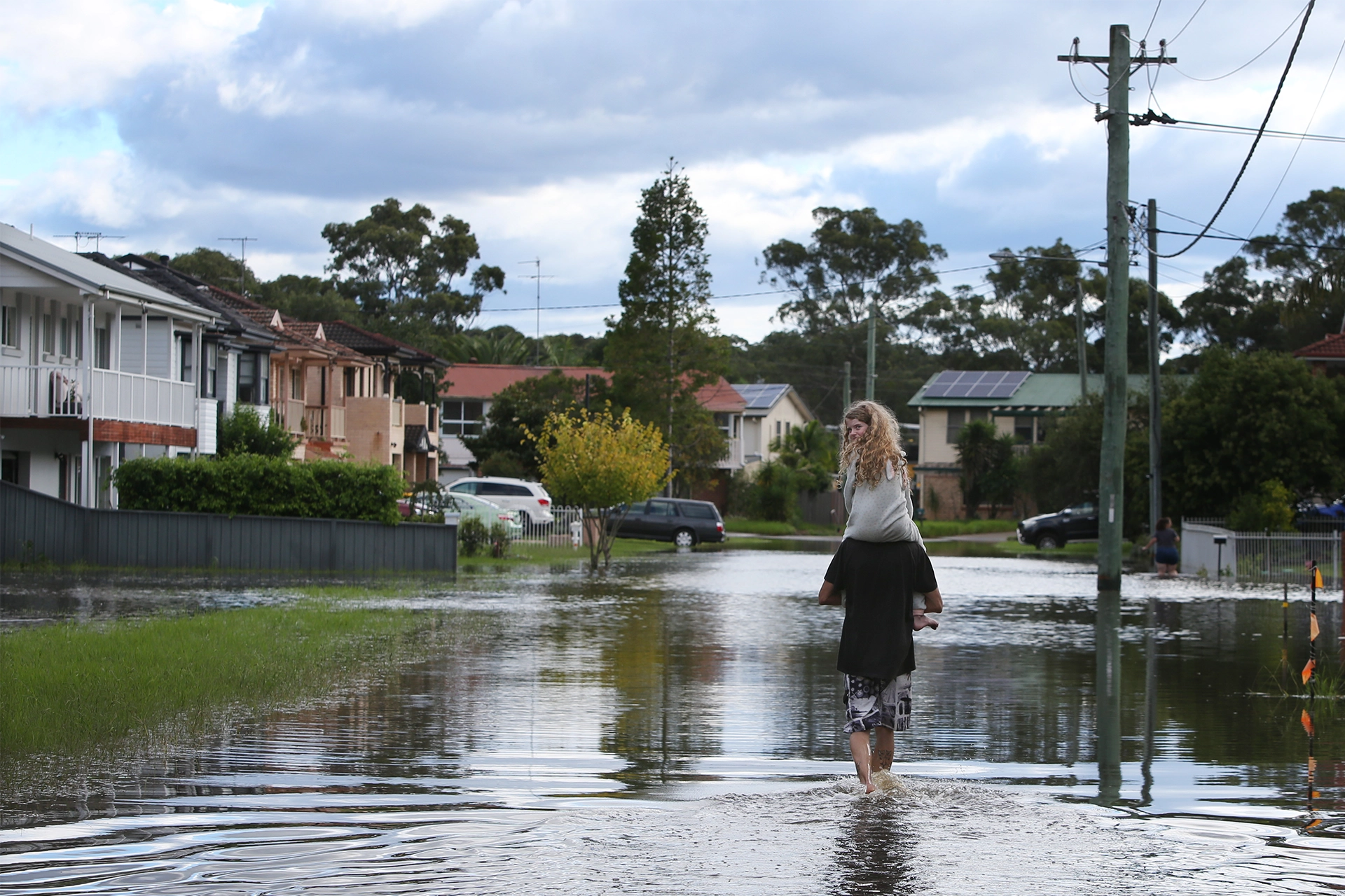 Man walking through a flooded suburban street with daughter on his shoulders