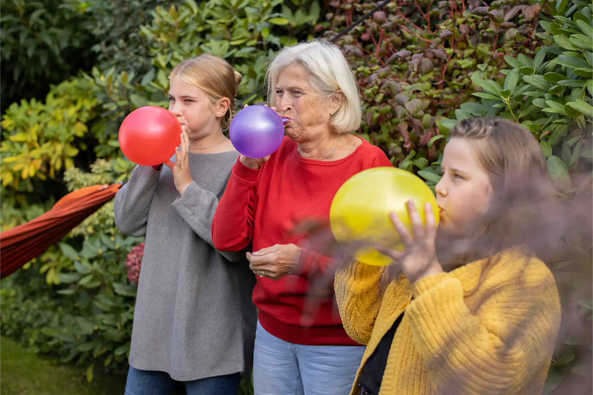 Senior woman with two children blowing up balloons in a garden