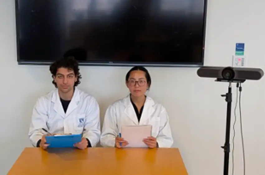 Two people in a white room wearing lab coats and serious expressions.