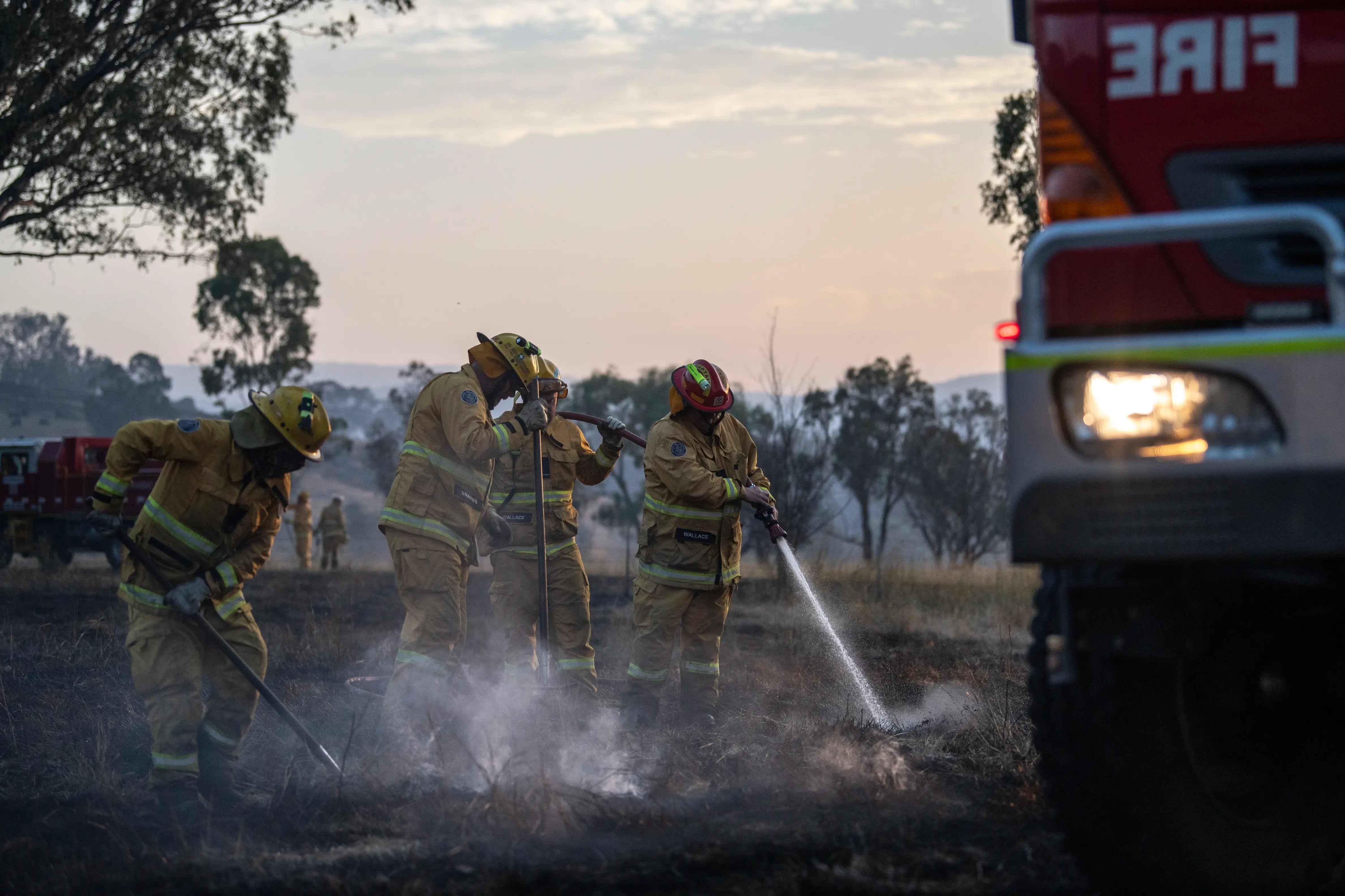 Four Country Fire Authority members hosing down a simmering grassfire at sunset
