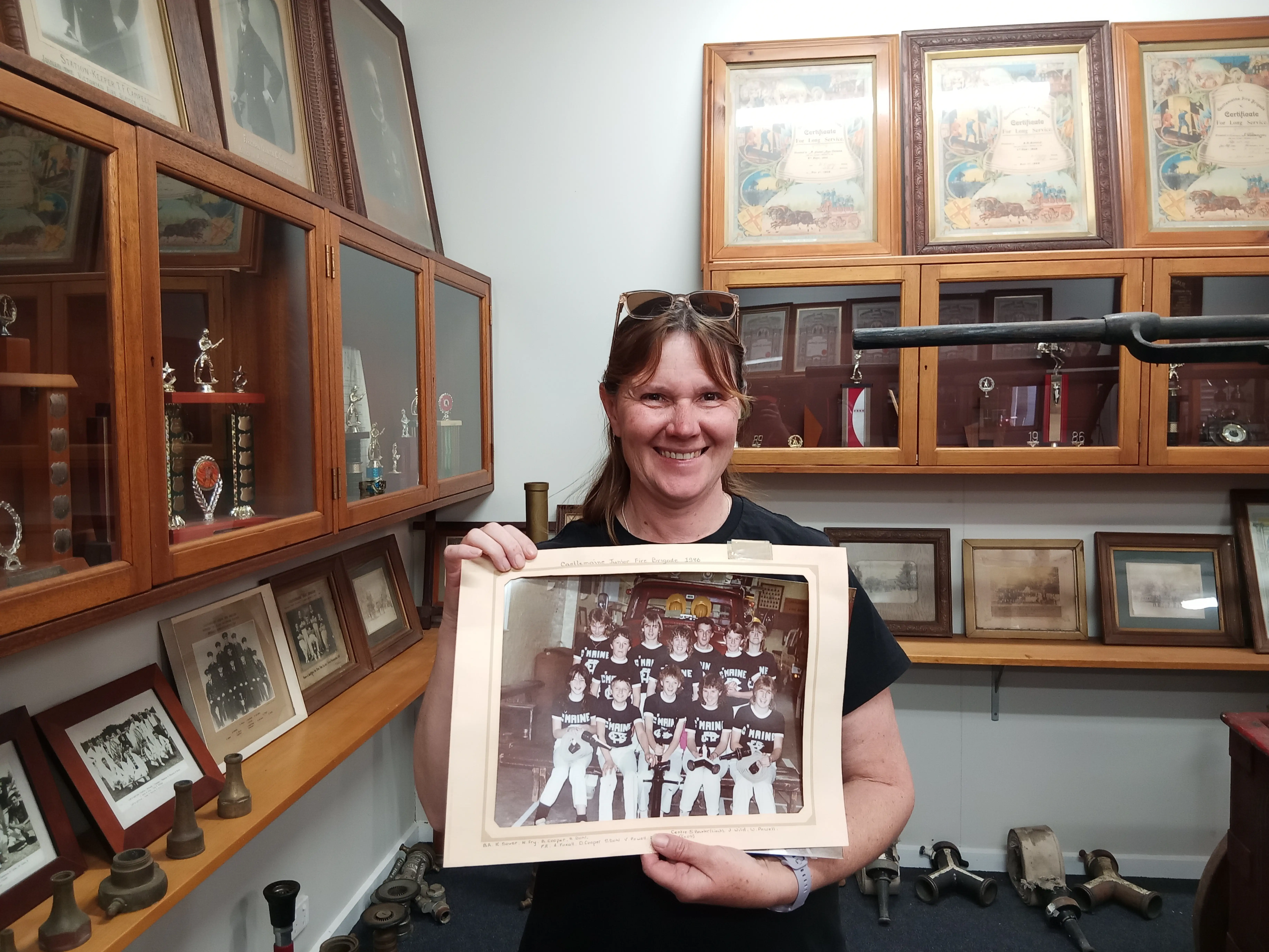 A woman smiles holding a laminated photo of junior members of the volunteer fire brigade