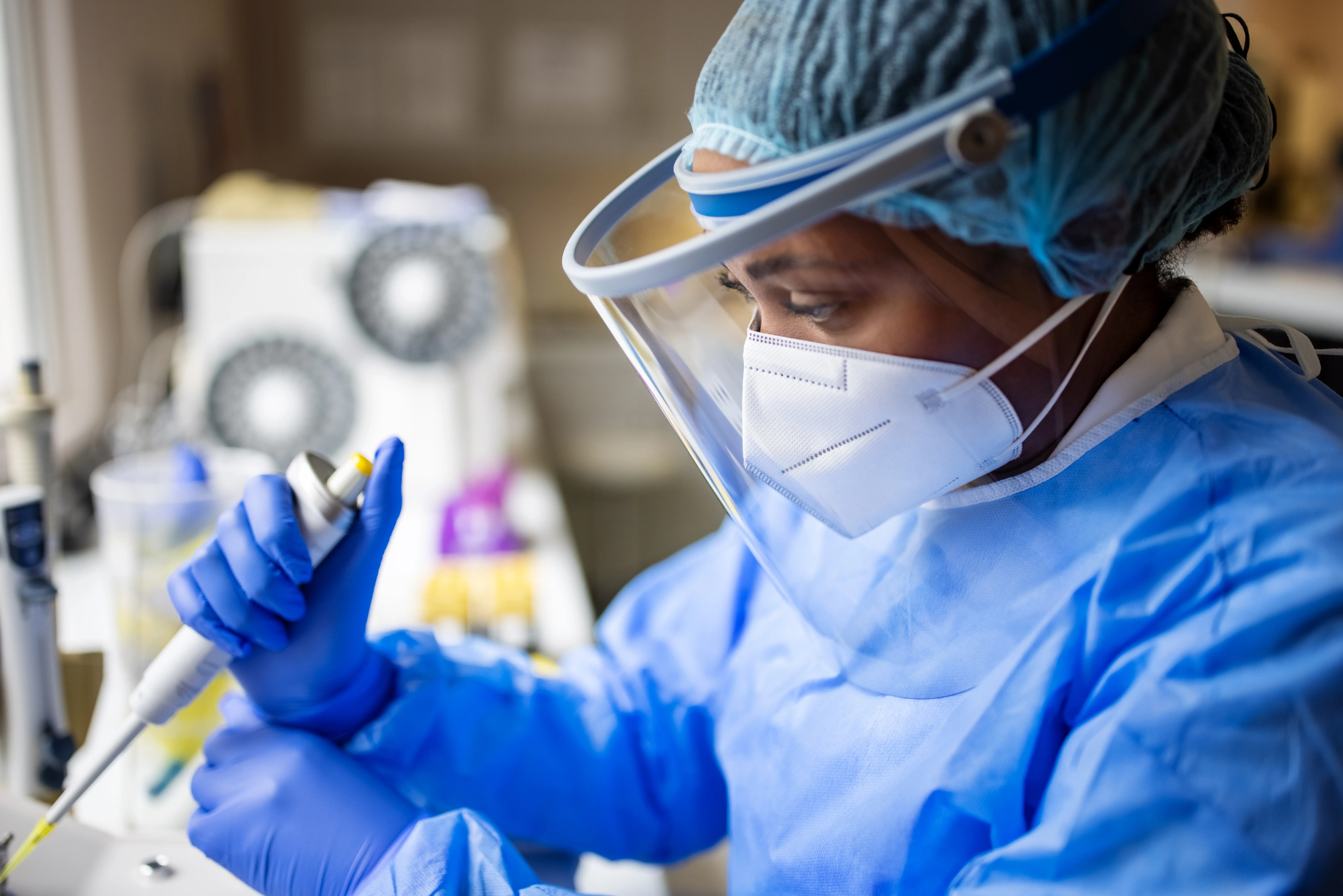 A female doctor wearing full PPE suit, face mask, and face shield working with pathogen samples in lab.