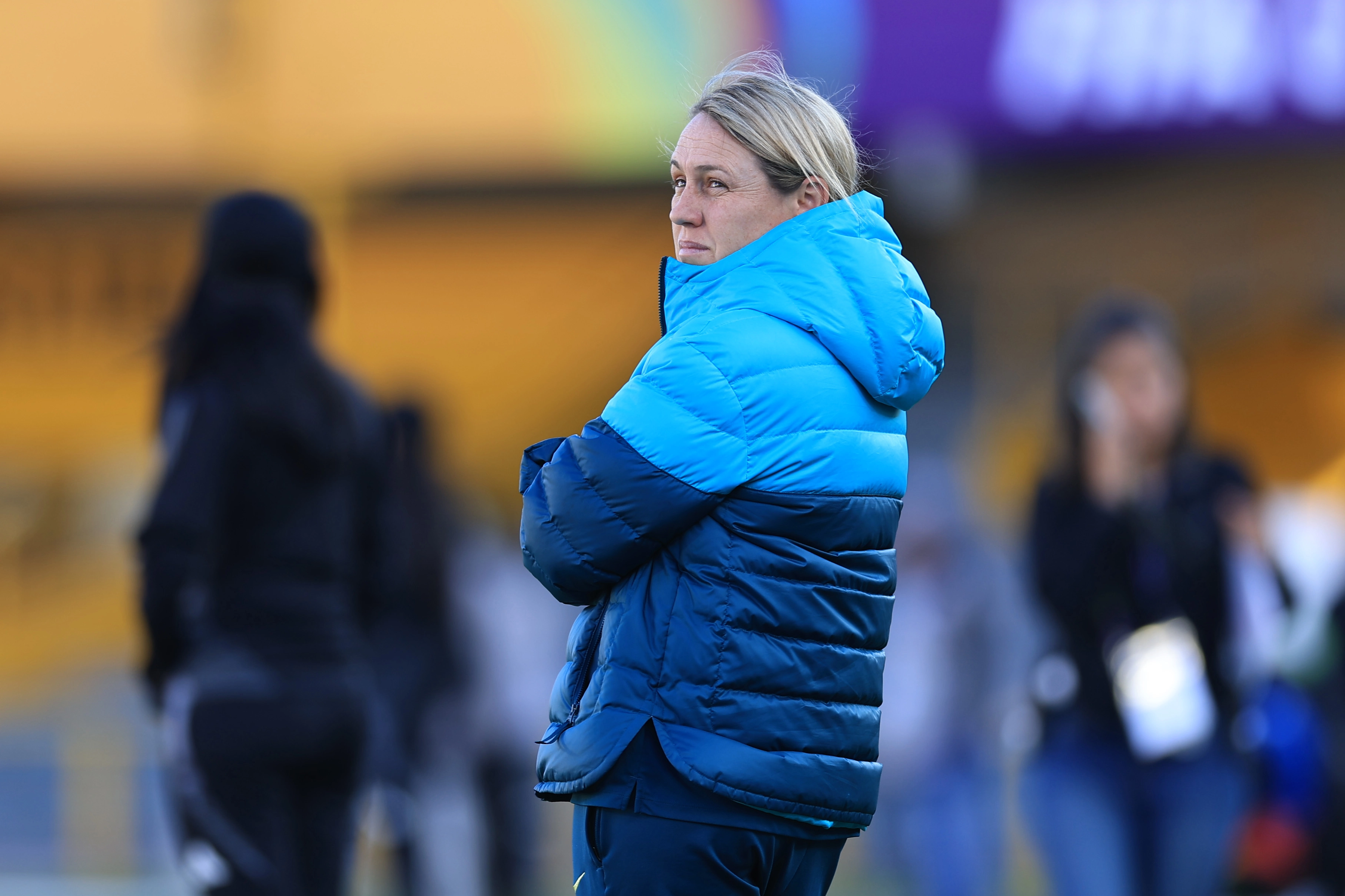 Leah Blayney in a light blue and navy puffer jacket watches a game from the sidelines with a concerned expression