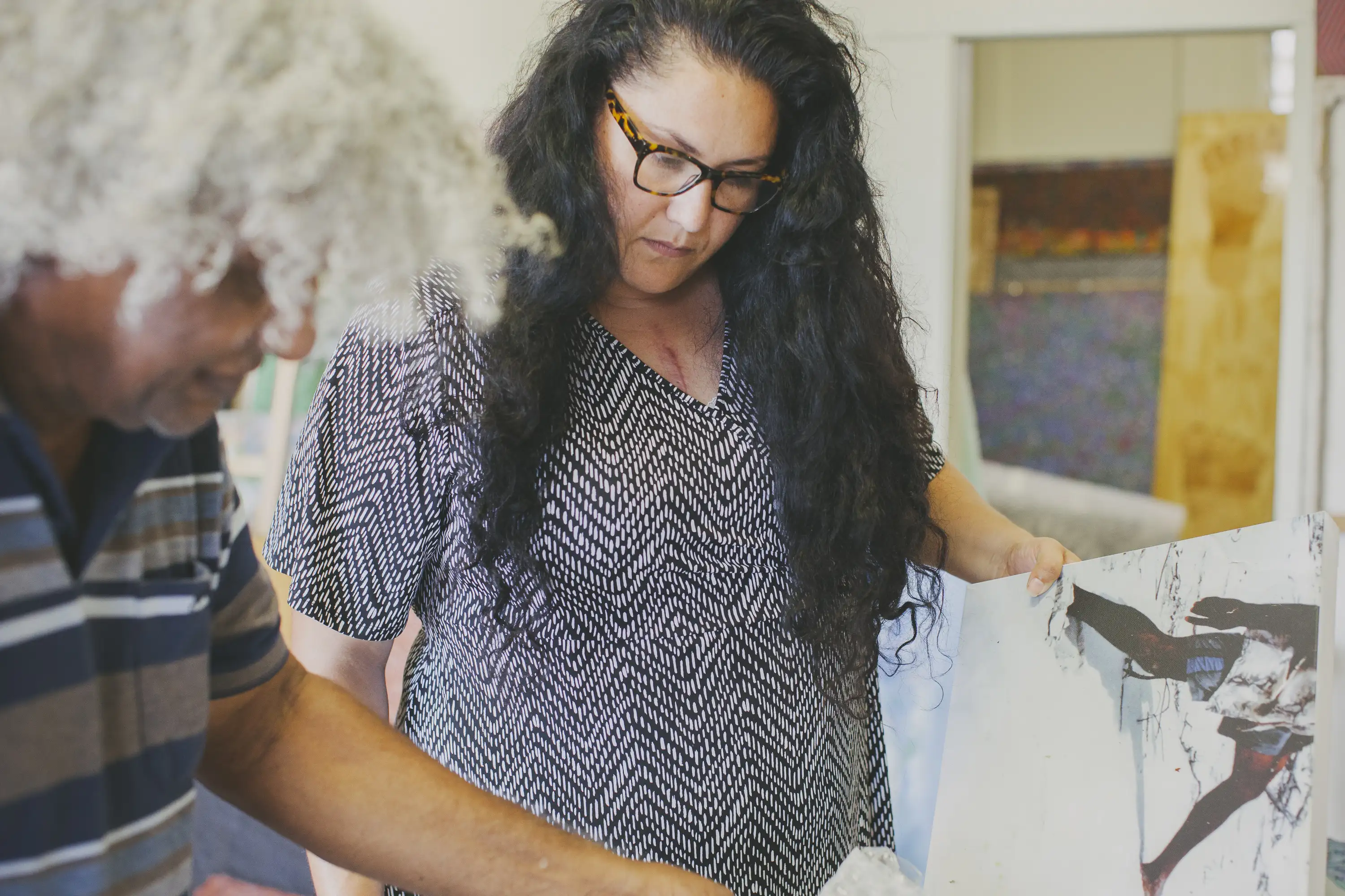 An Aboriginal woman inspects artwork in an Indigenous artist's studio