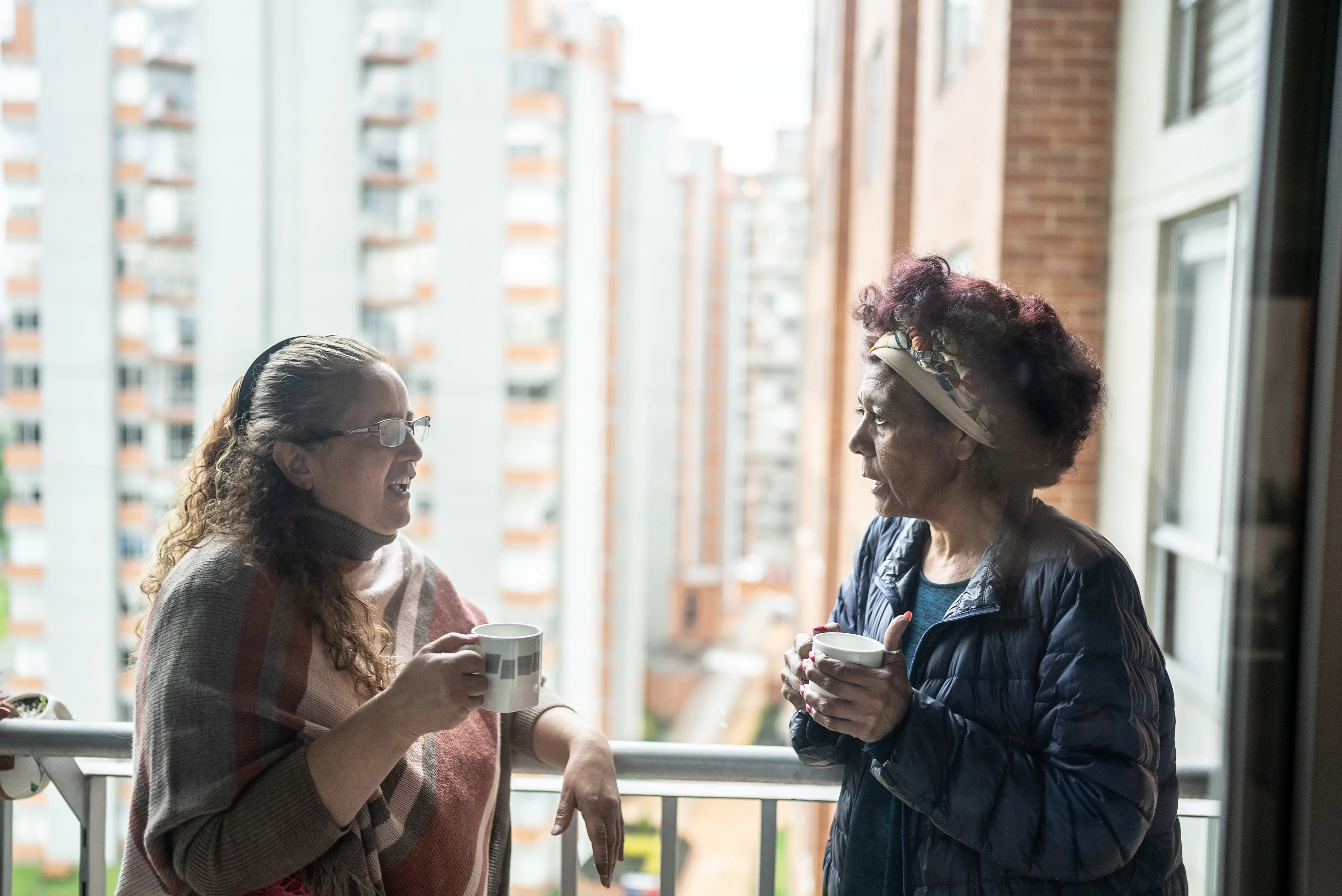 Two female neighbours drinking coffee on a balcony