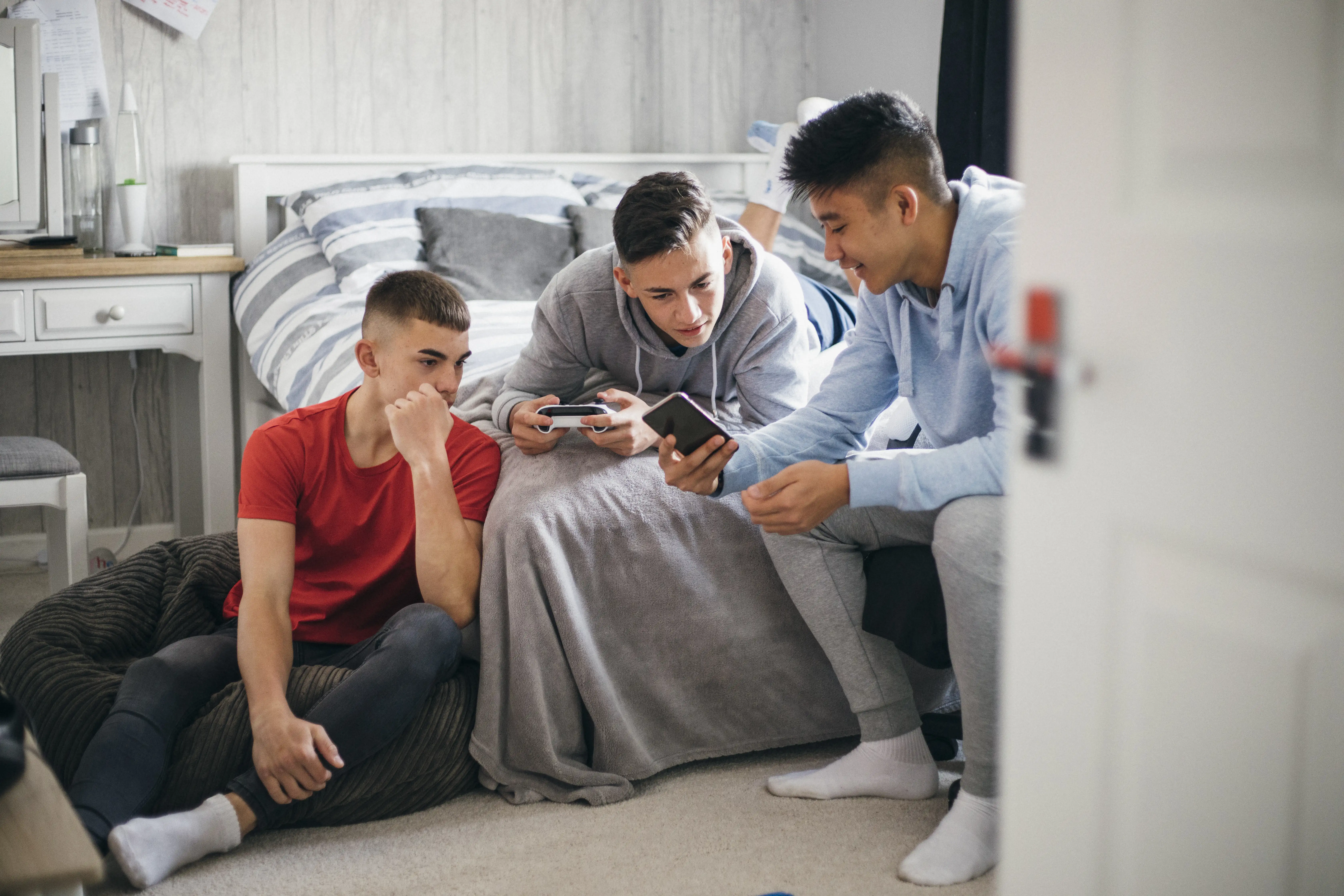 Three teenage boys gaming and looking at their phones