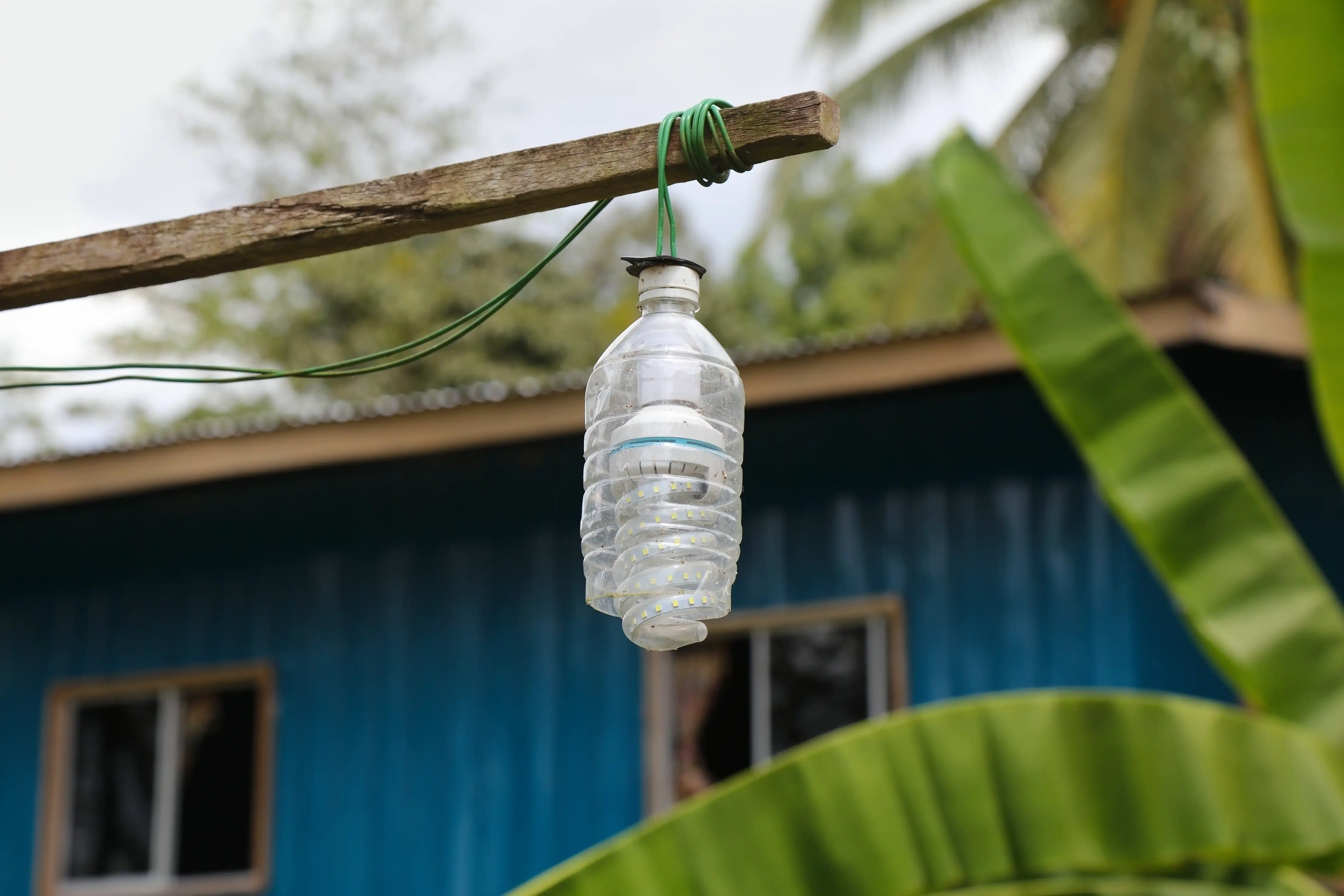 A light bulb hanging on a piece of wood covered by plastic from a bottle as a makeshift outdoor light