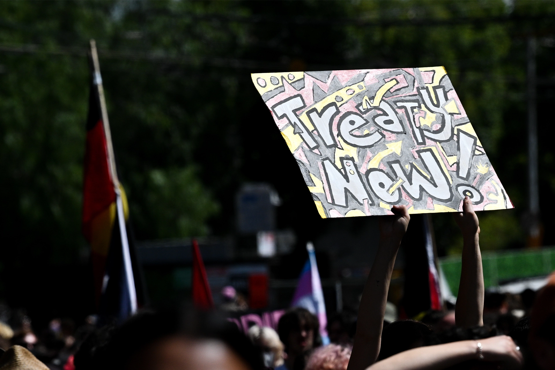 A group marching with an Aboriginal flag and a sign that says 