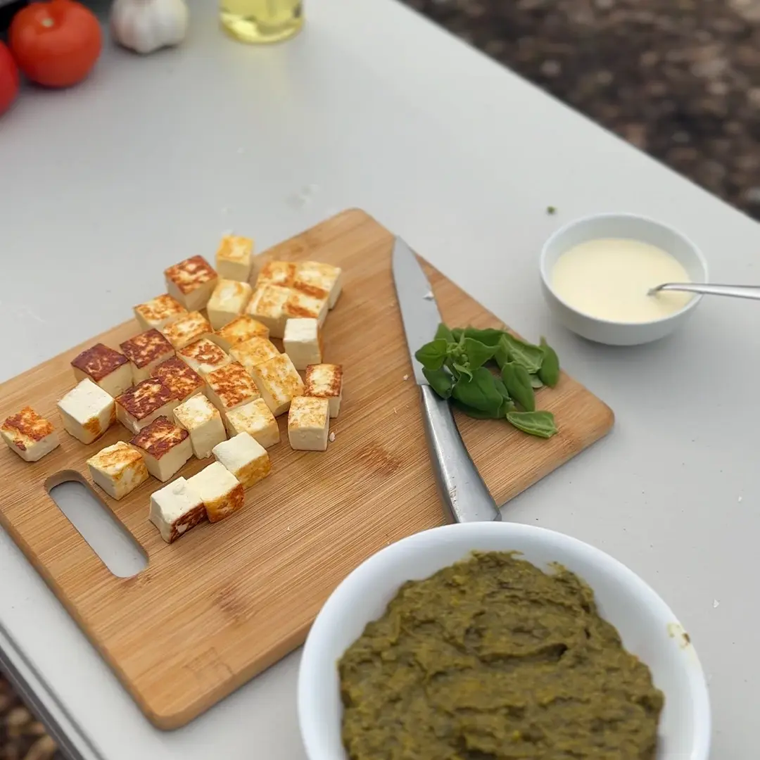 Recently pan fried fetta cubes on a wooden chopping board surrounded by various ingredients 