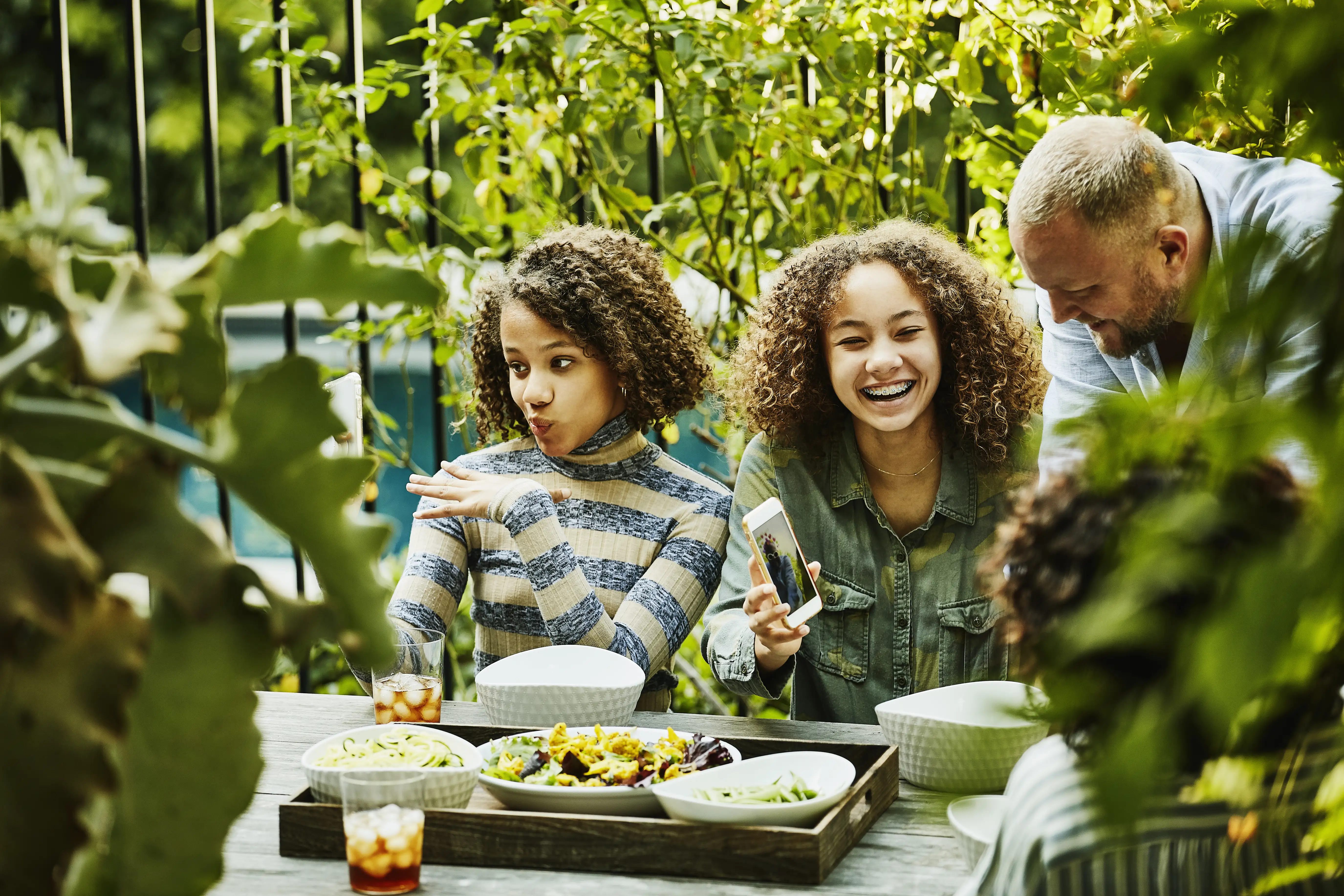 Laughing family playing with photos on smart phones during dinner