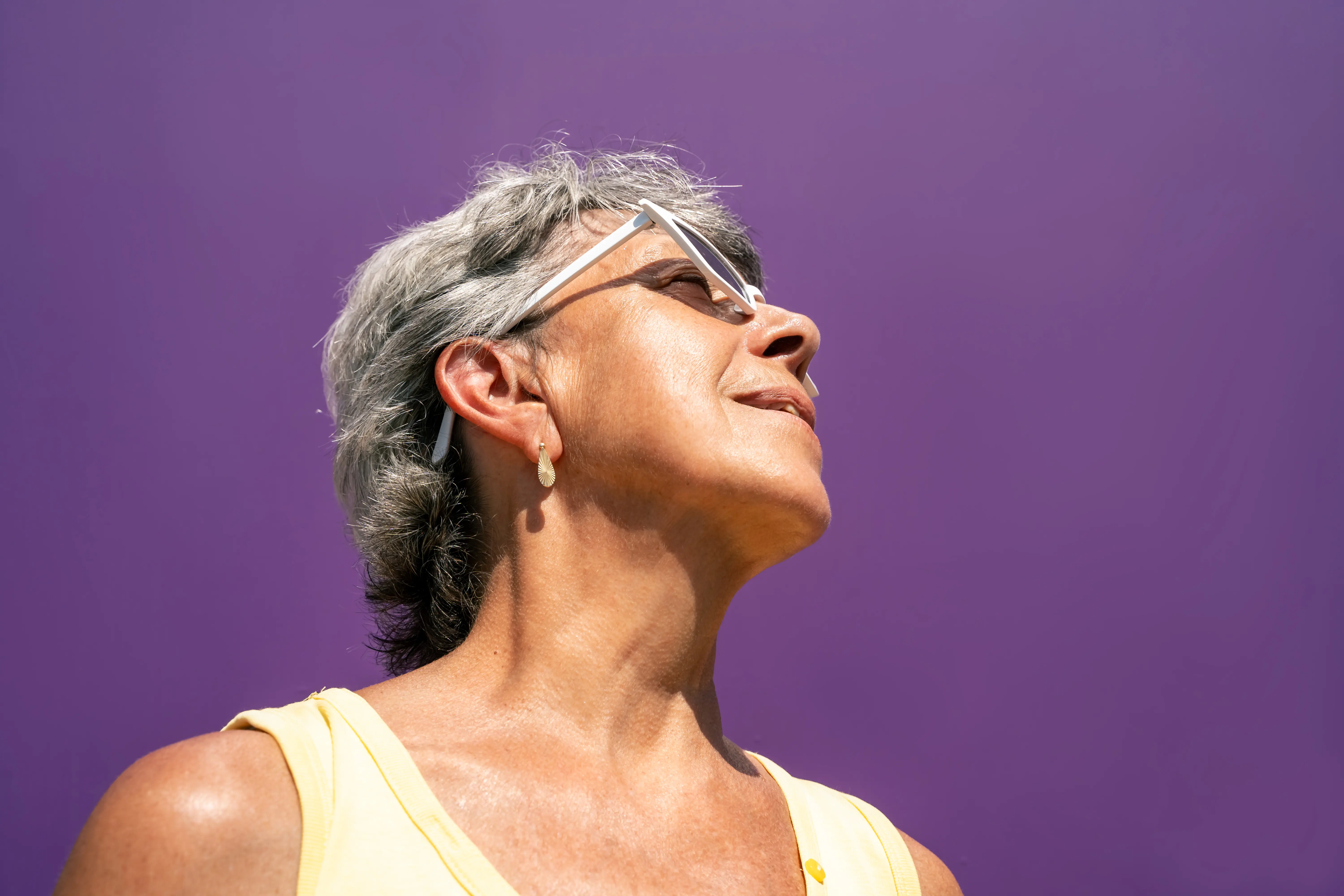 Portrait of senior woman in sunglasses on bright purple background, view from below