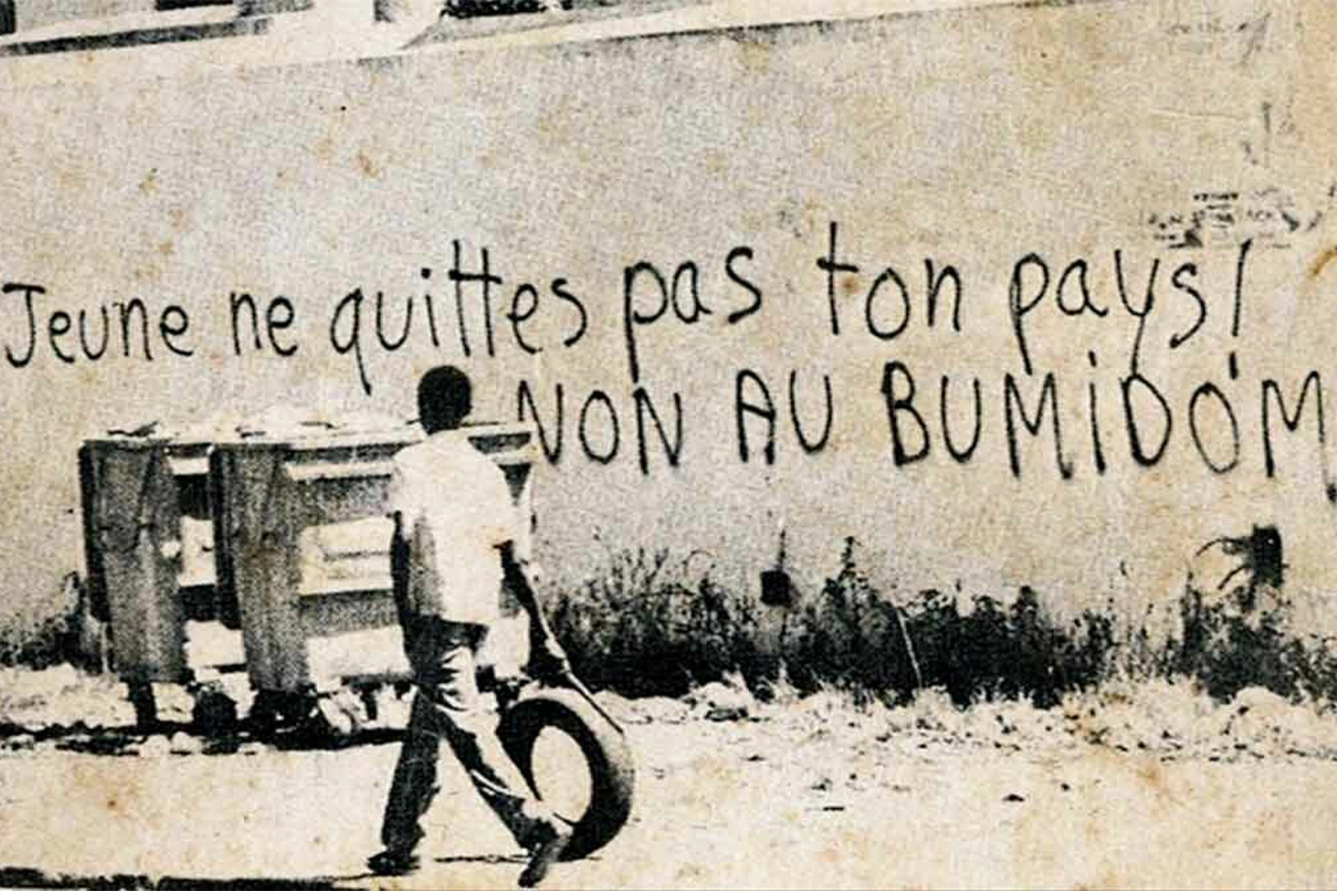 Boy pushing a tyre past a graffitied wall