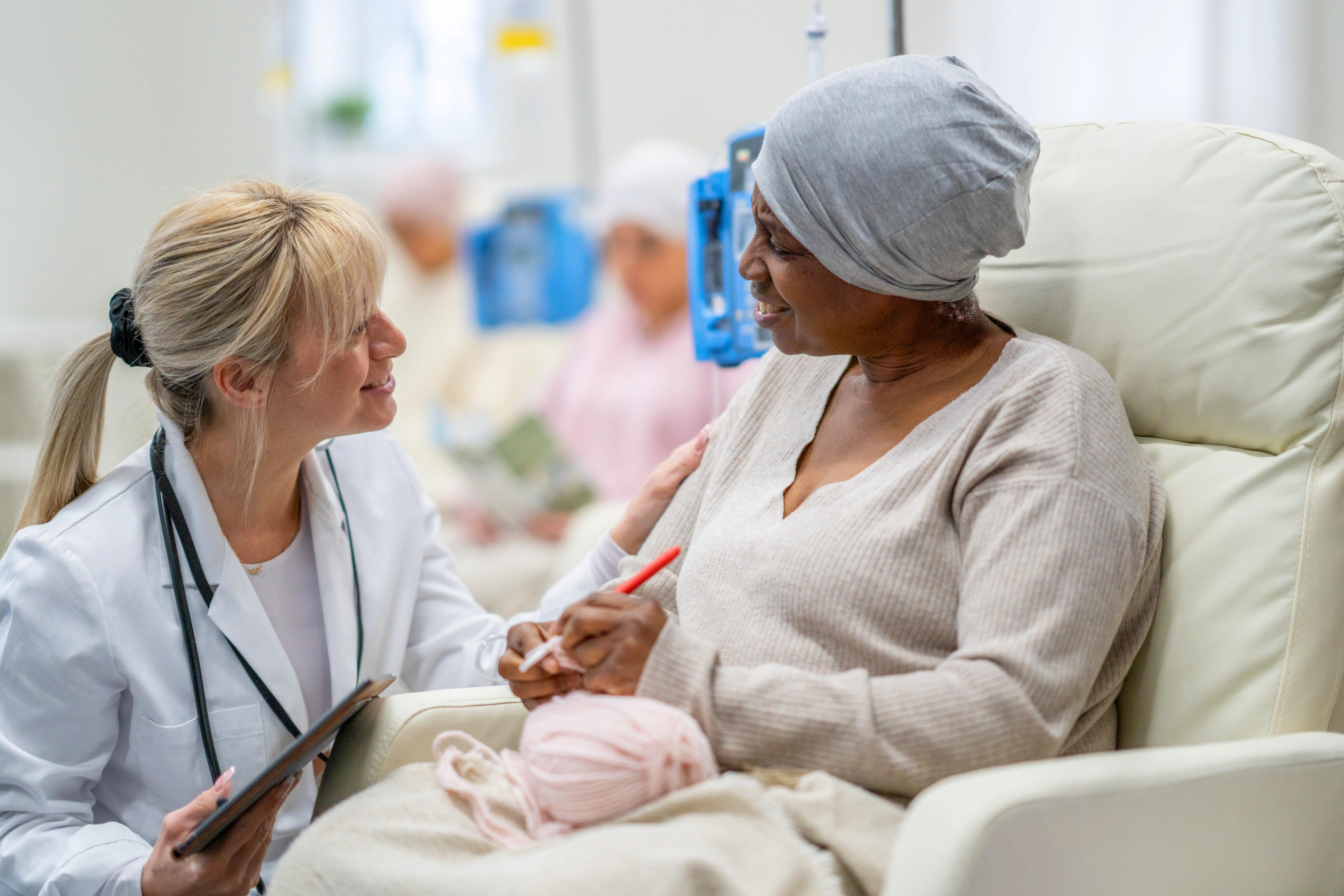 A female oncologist kneeling down in front of a female patient in a cancer clinic