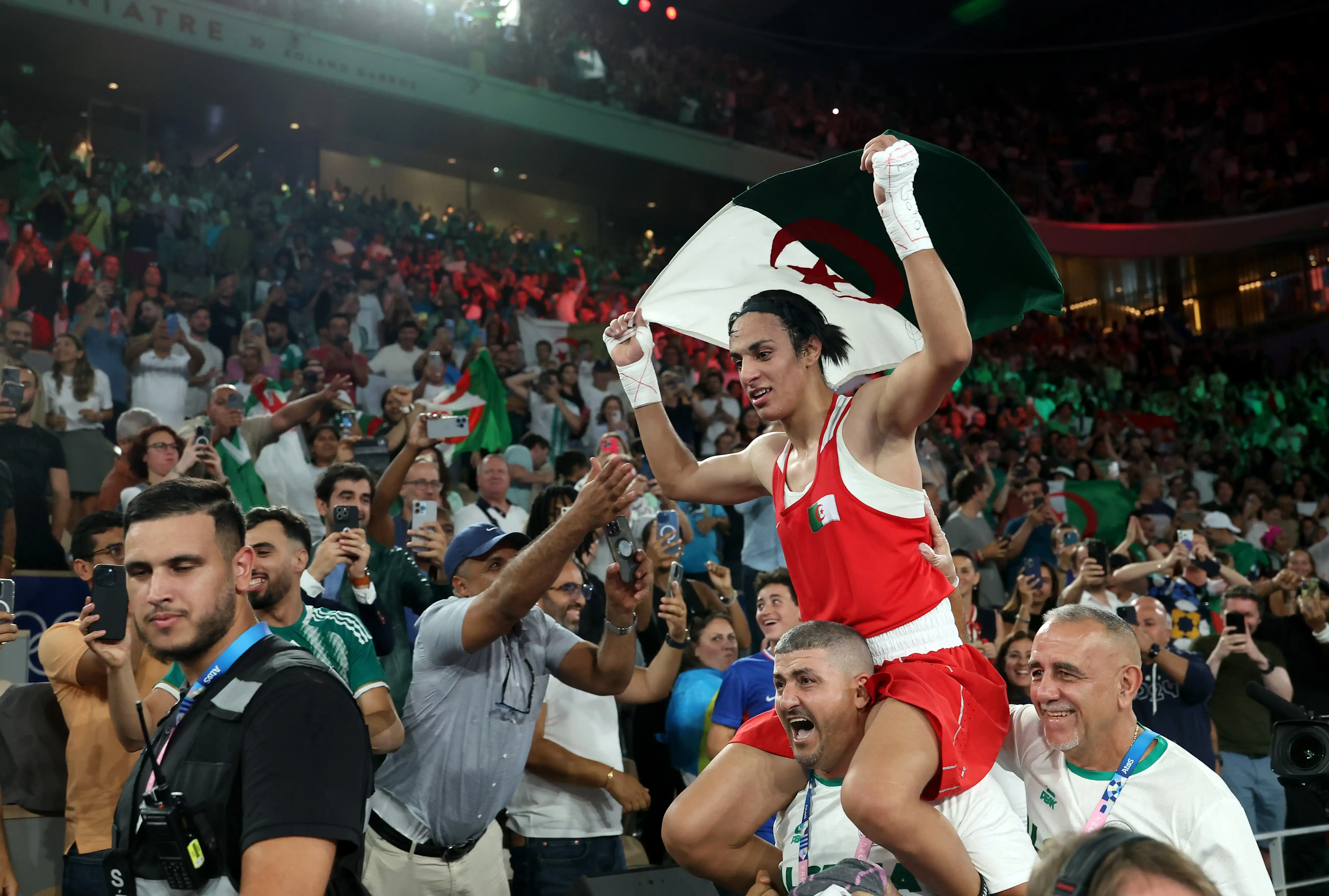 Olympian Imane Khelif of Algeria on the shoulders of her coach as she is carried away from the boxing ring with her country’s flag in her hands