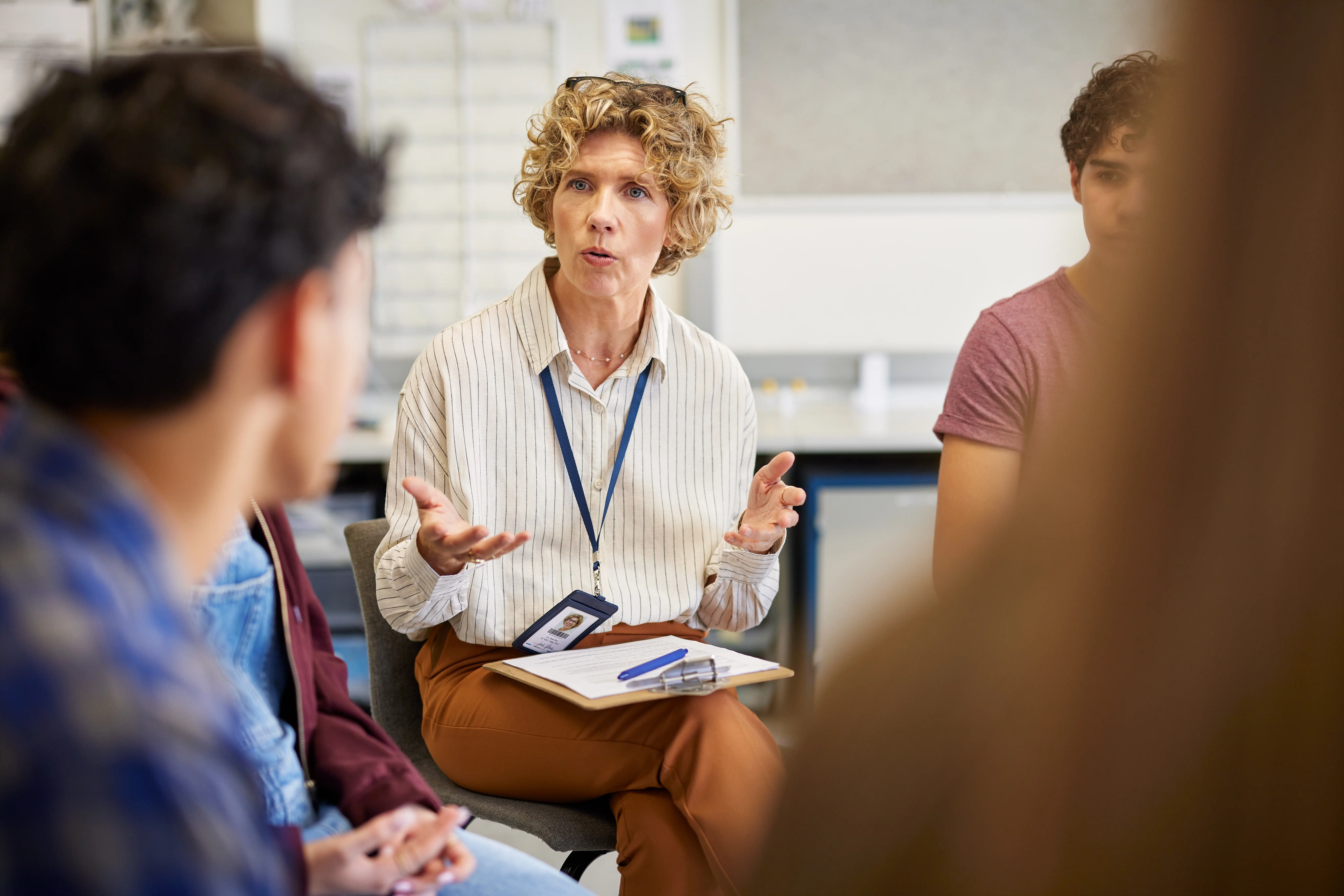 A mature female teacher speaking during a focused group session with students in classroom
