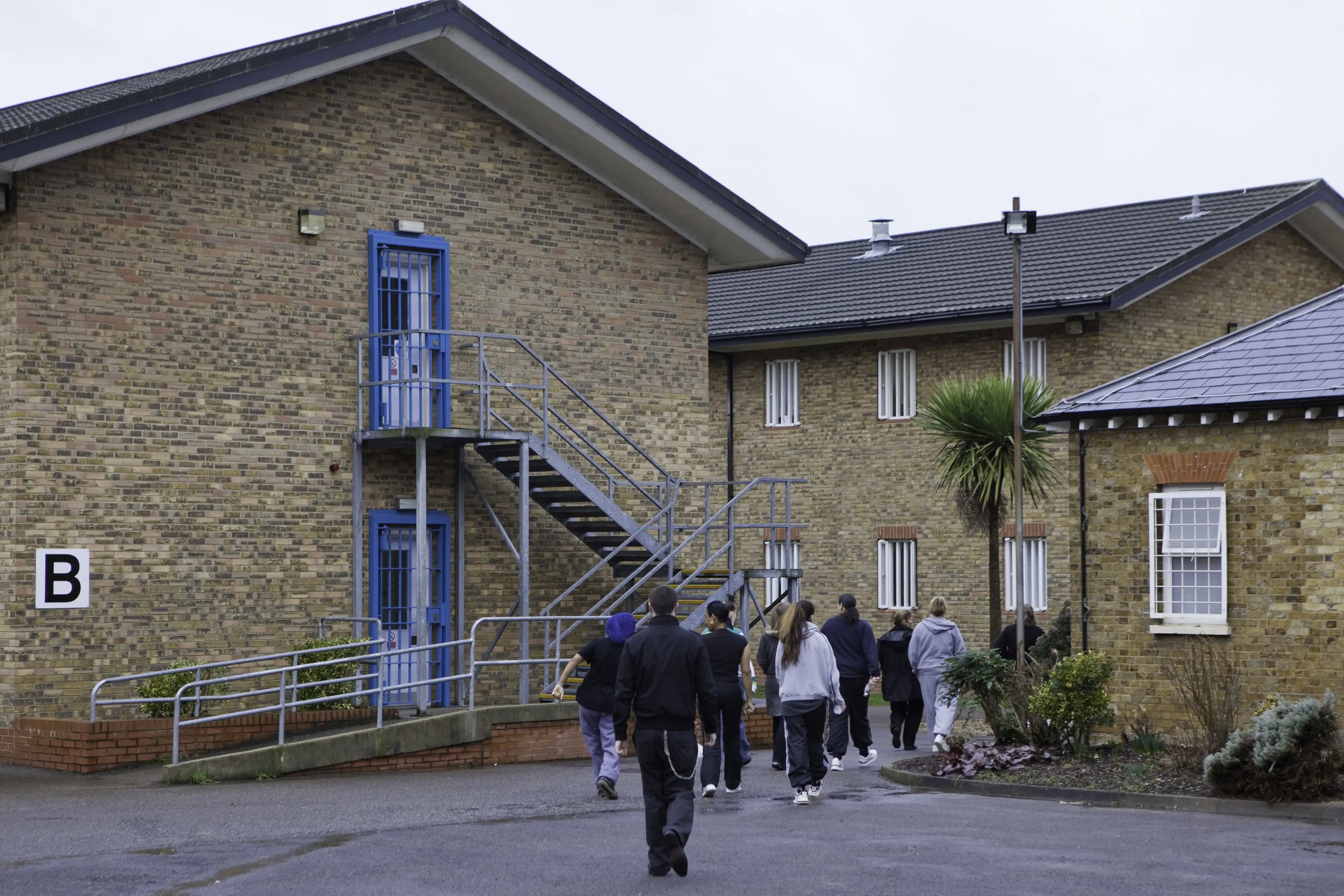 Women are escorted through a prison outdoor area by a guard