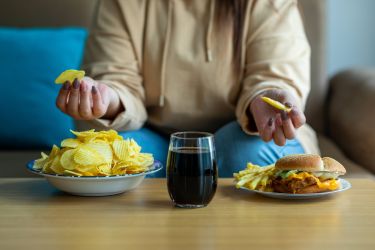 An anonymous woman sitting in front of bowls of chips and a glass of cola