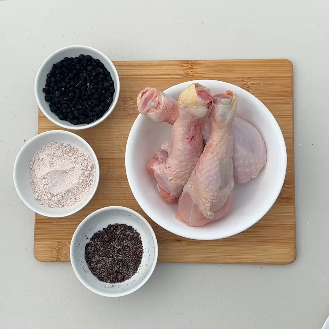 Raw chicken in a bowl alongside three smaller bowls of seasoning