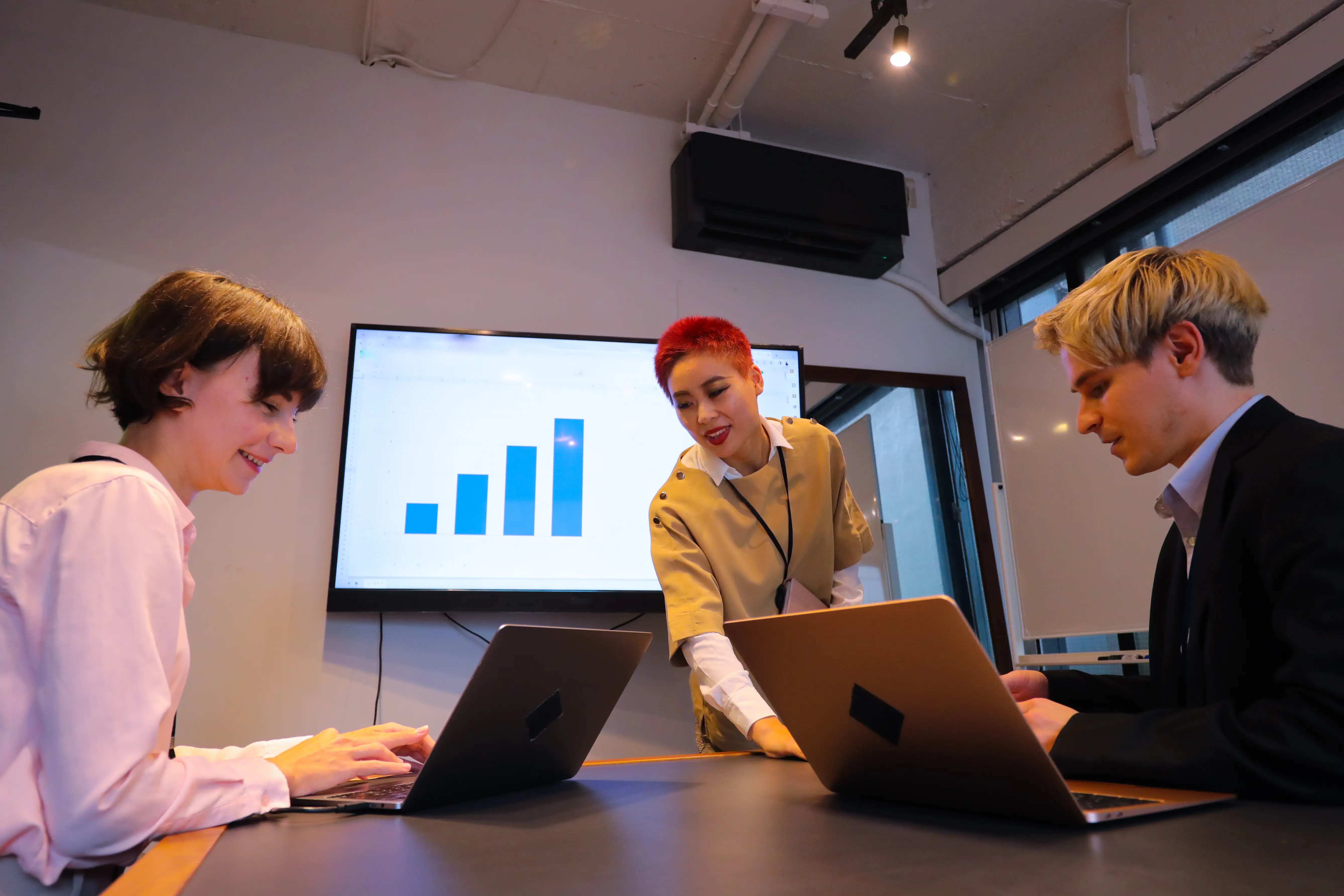 Three diverse people in a meeting room organising their slides