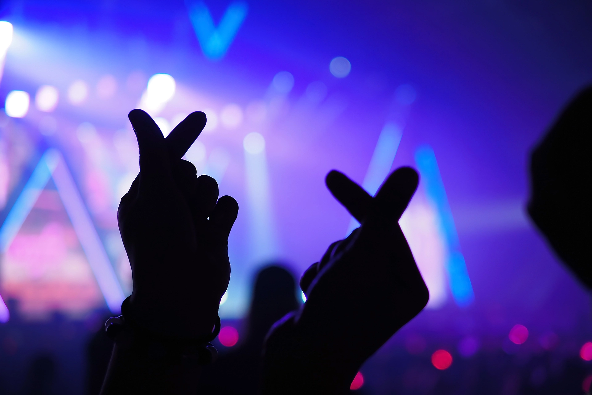 Silhouettes of hands in the air making a love heart shape with fingers at a music concert