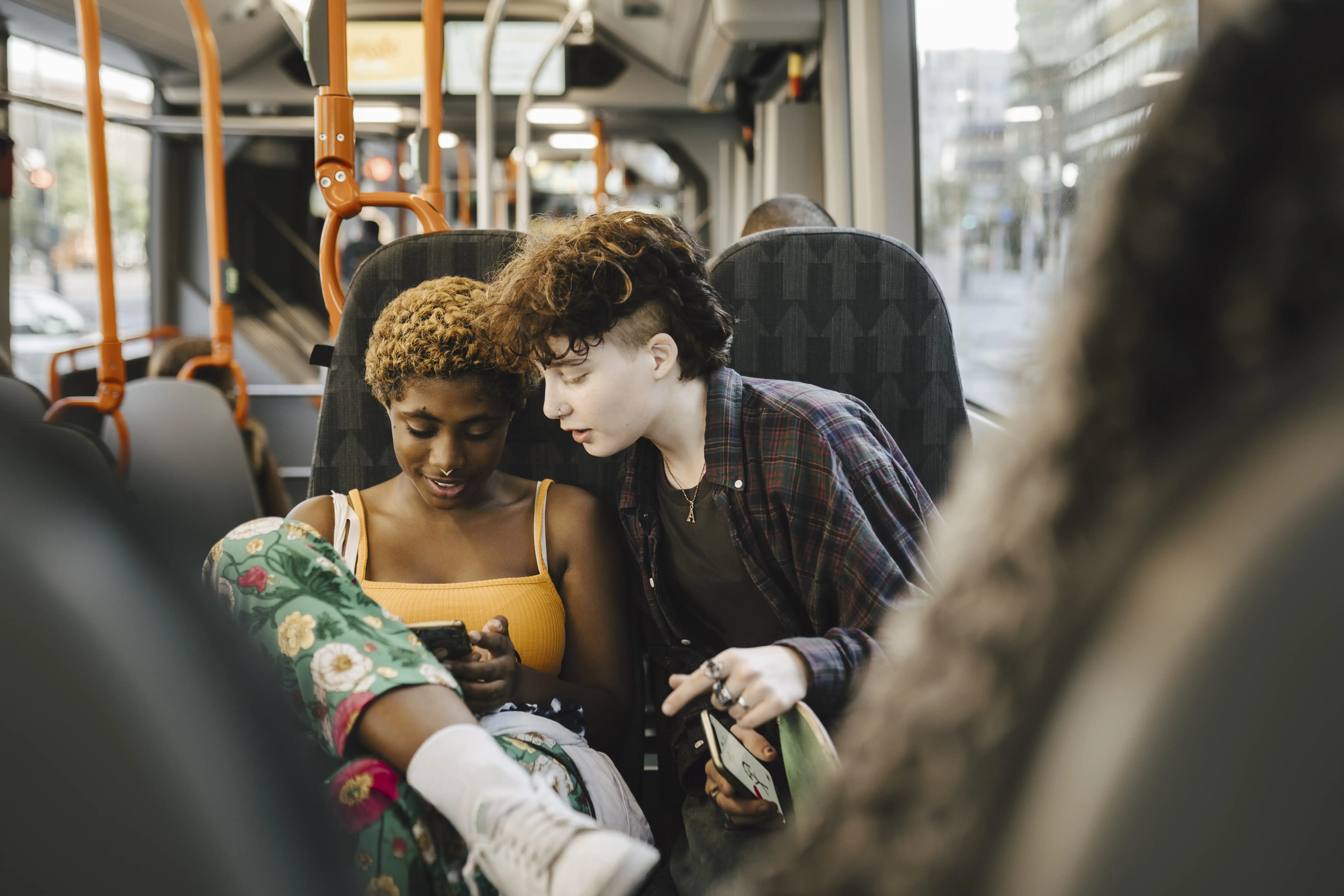 Teenage boy looking over the shoulder of a young non-binary woman at smart phone on bus