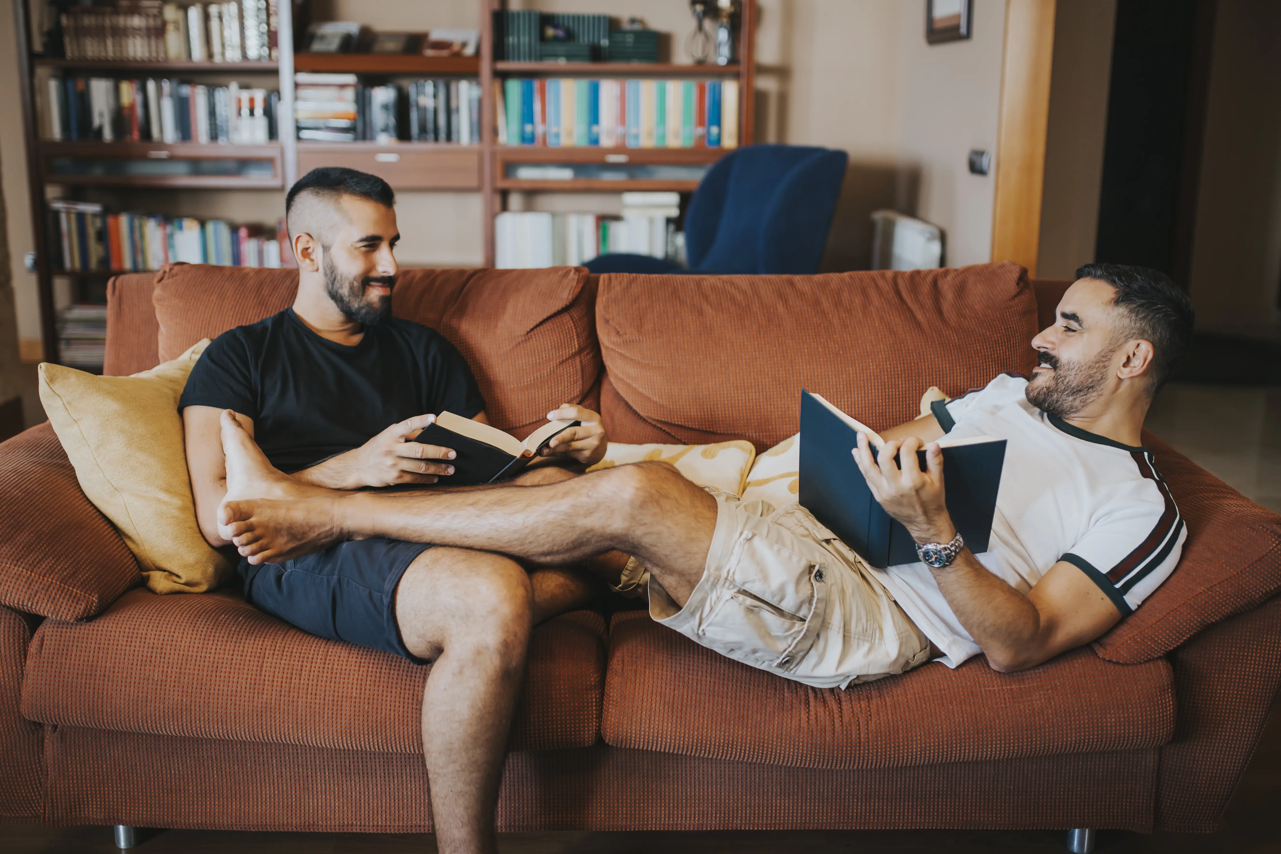 Gay couple reading on the sofa with their legs on each other 