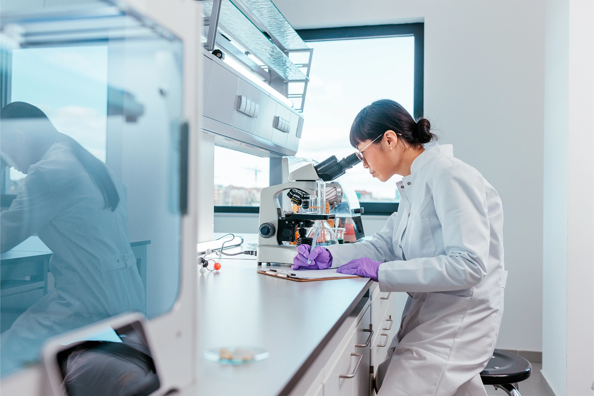 Asian female scientist looking through a microscope and writing