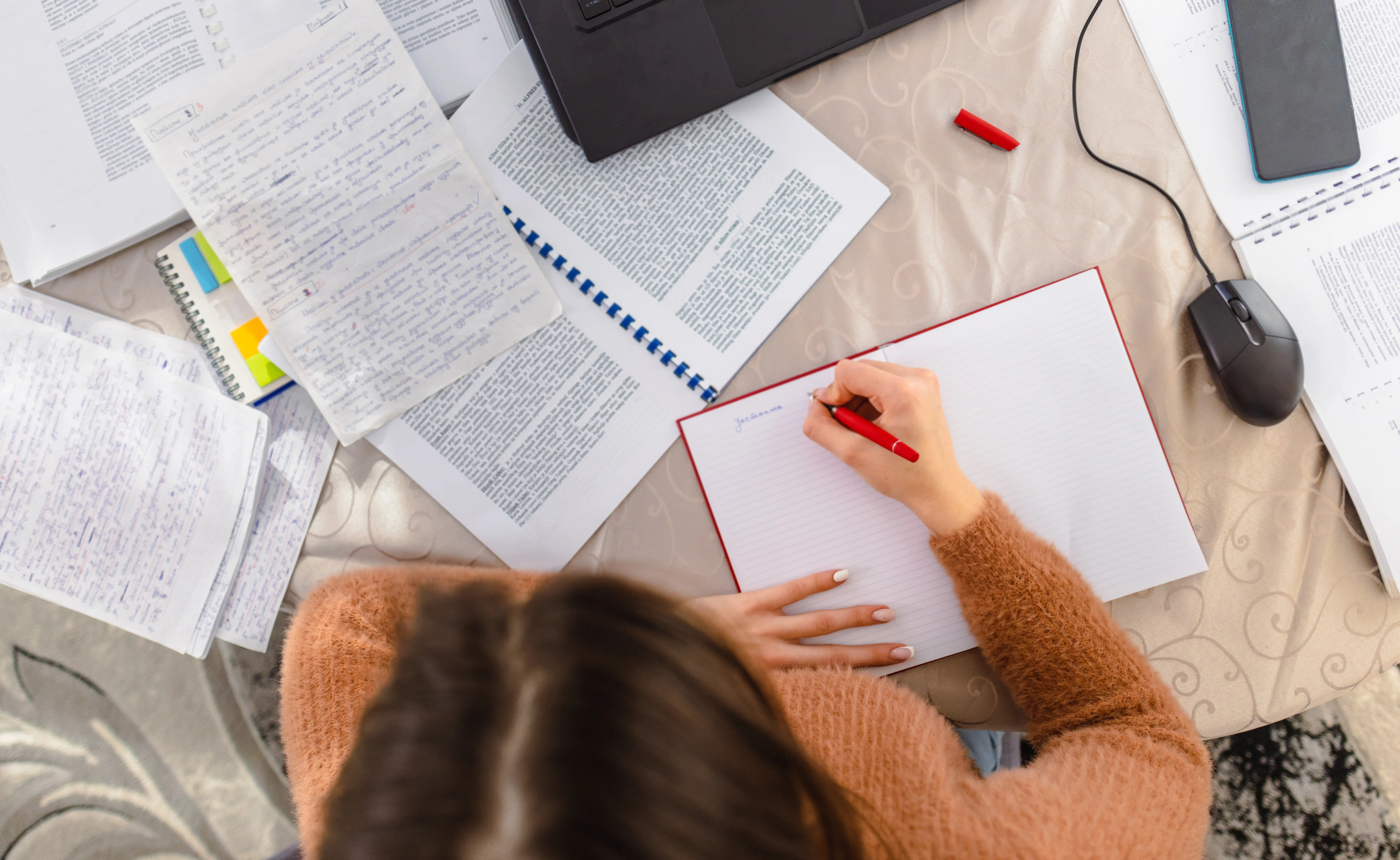 A young woman at a desk studying for an upcoming exam surrounded by notes.