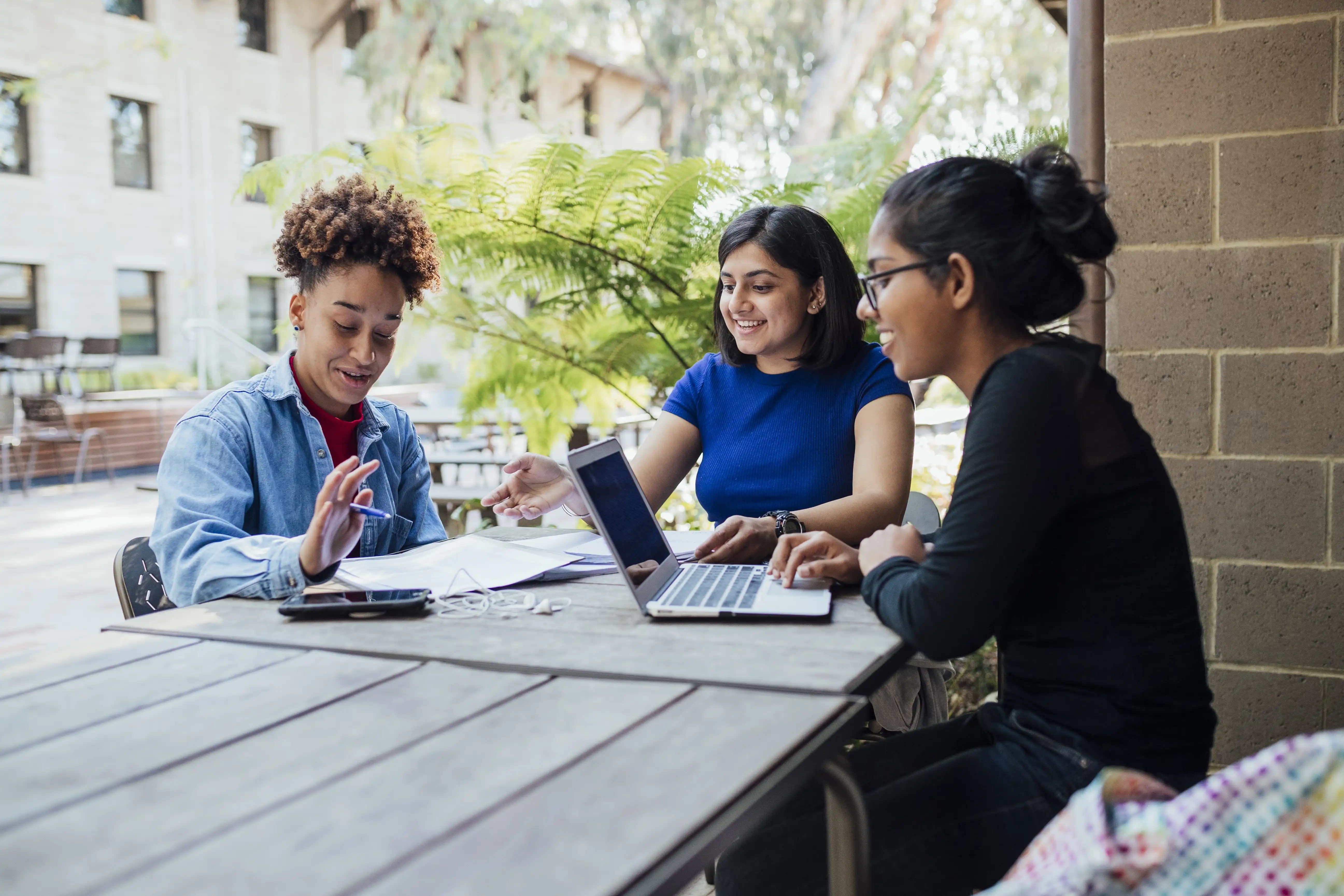 Three university students study together outside on campus