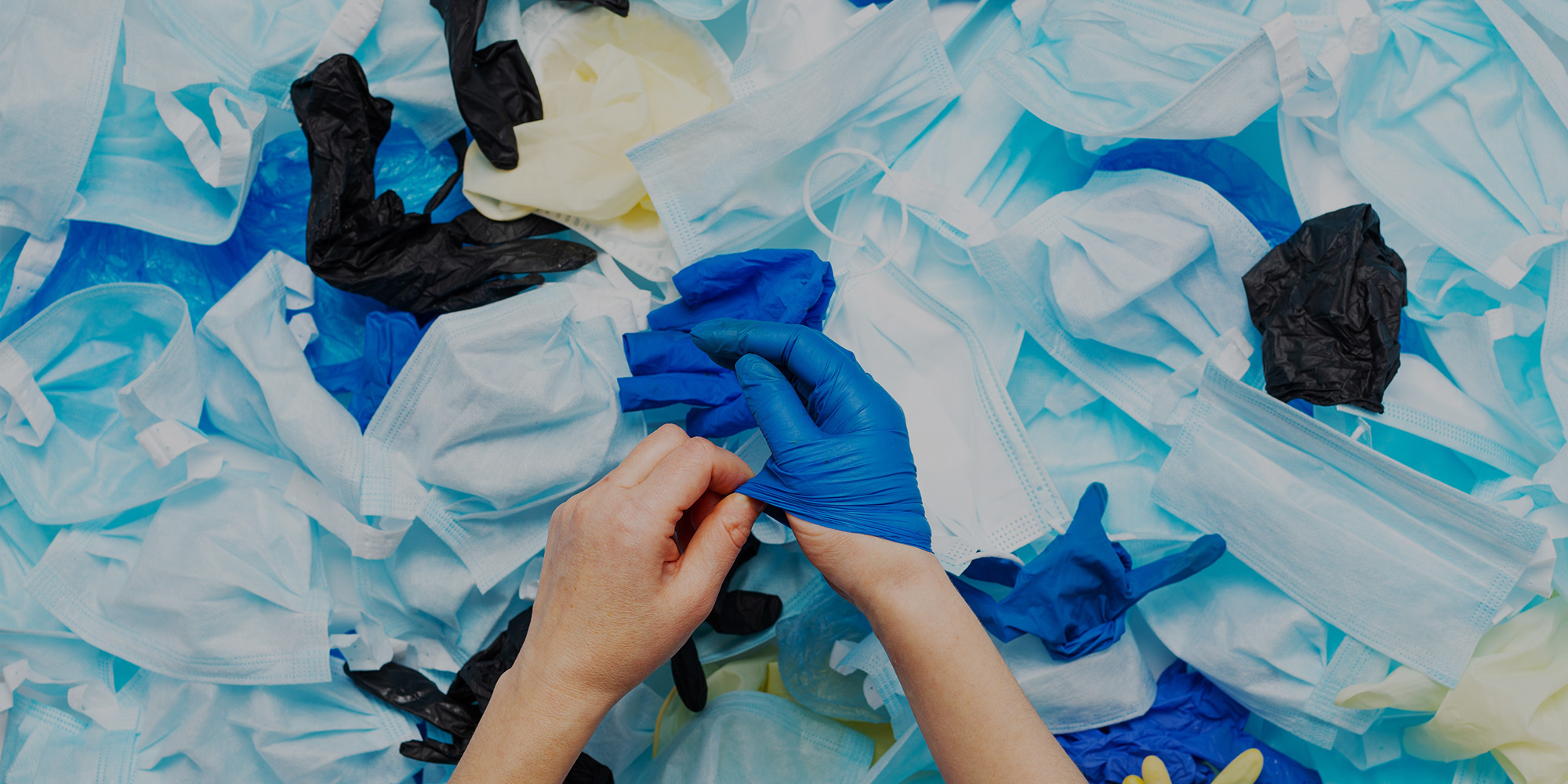 A person putting a glove on over a pile of disposable gloves