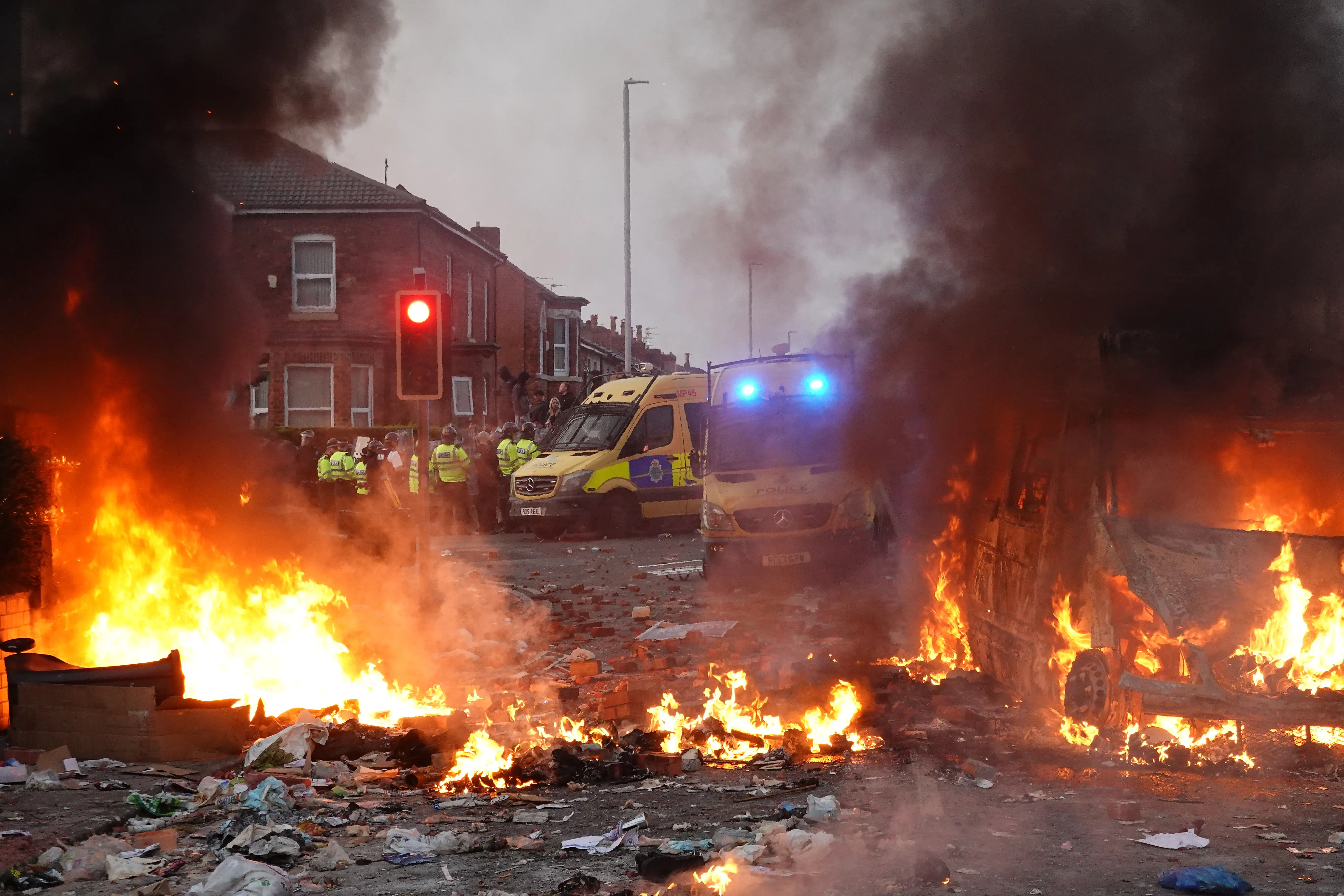 Riot police hold back protesters near a burning police vehicle