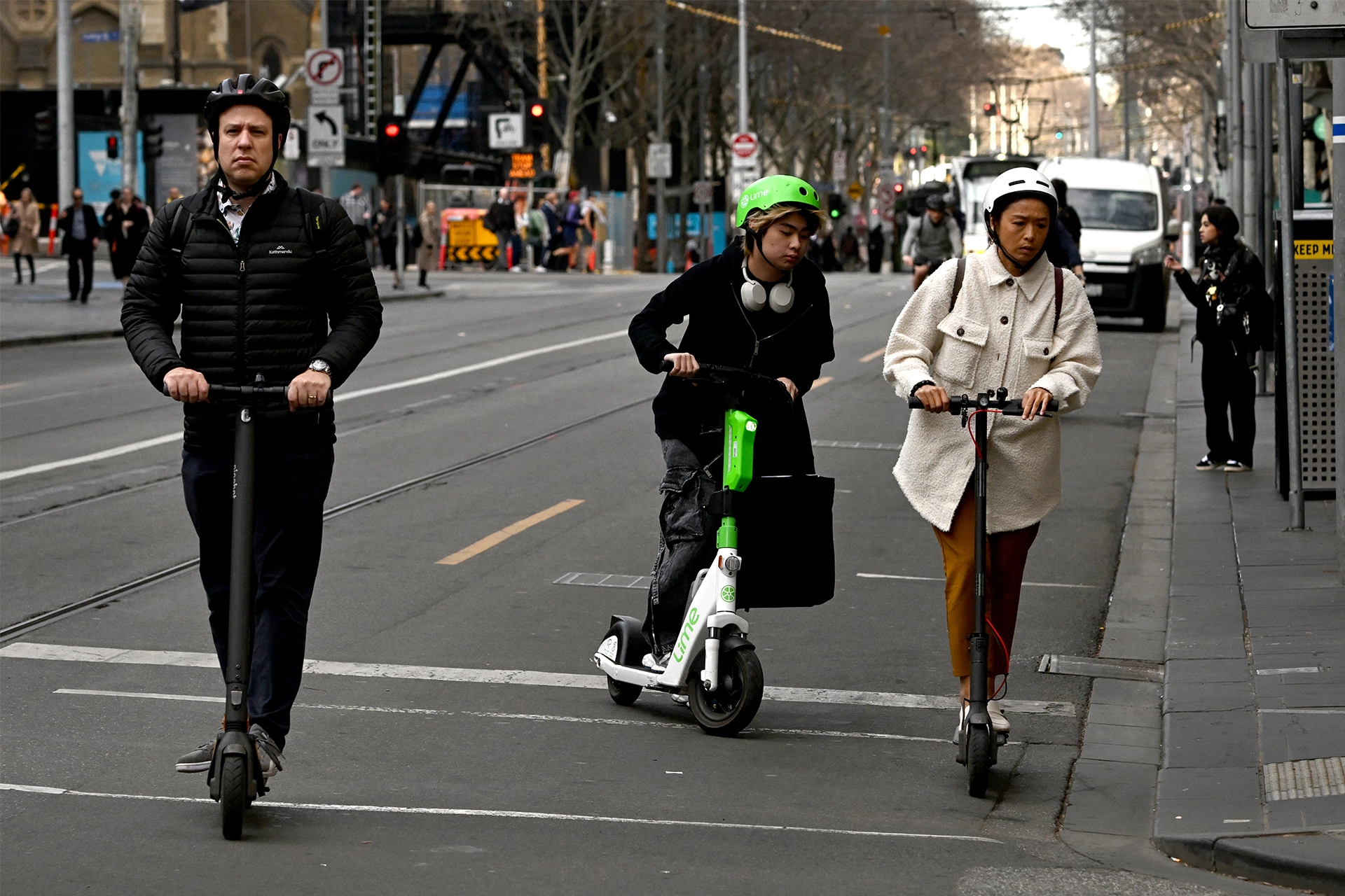 Three individuals riding e-scooters and wearing helmets in Melbourne CBD 