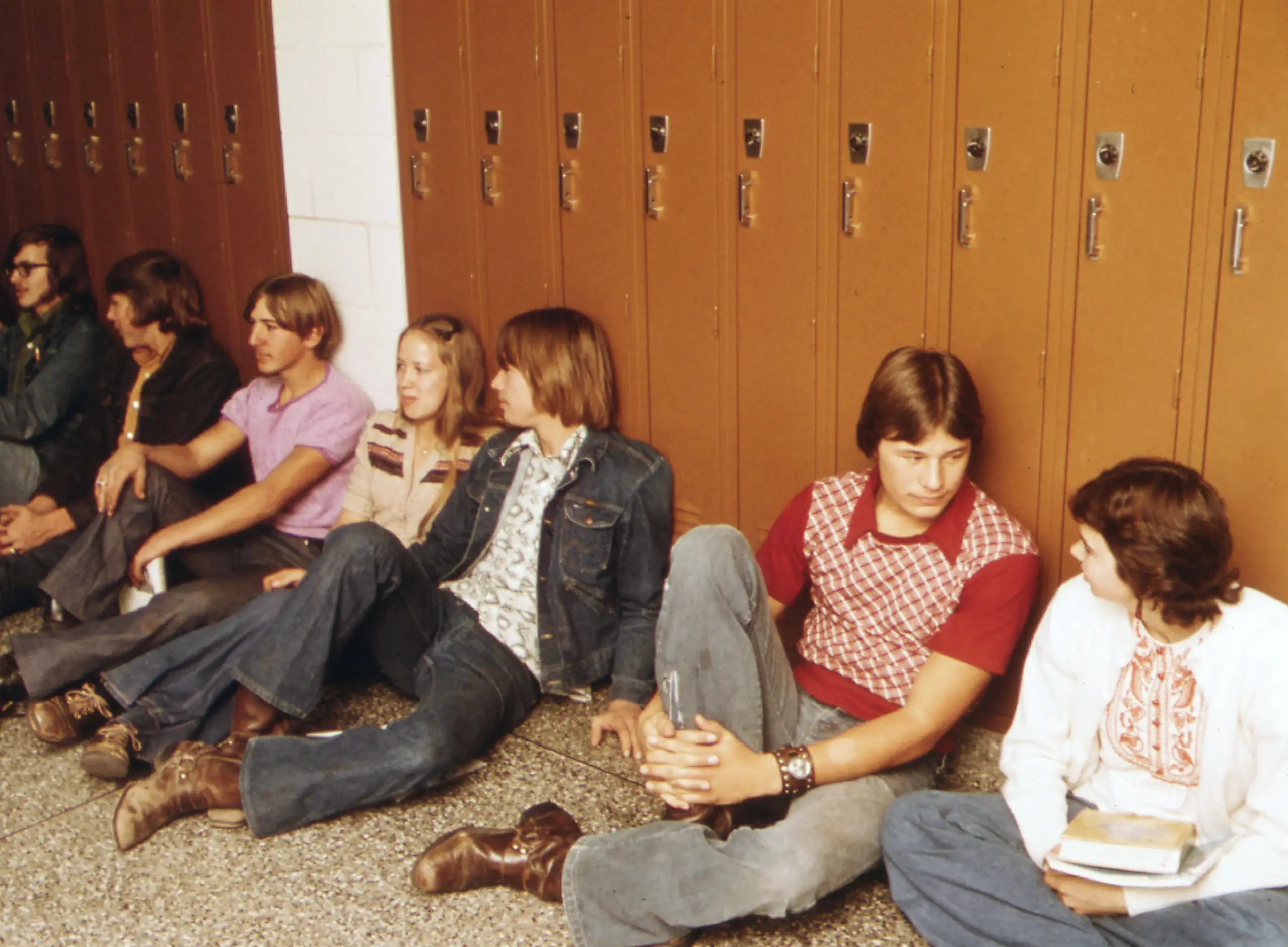 Teenagers resting against lockers in a high school hallway of the early 1970s