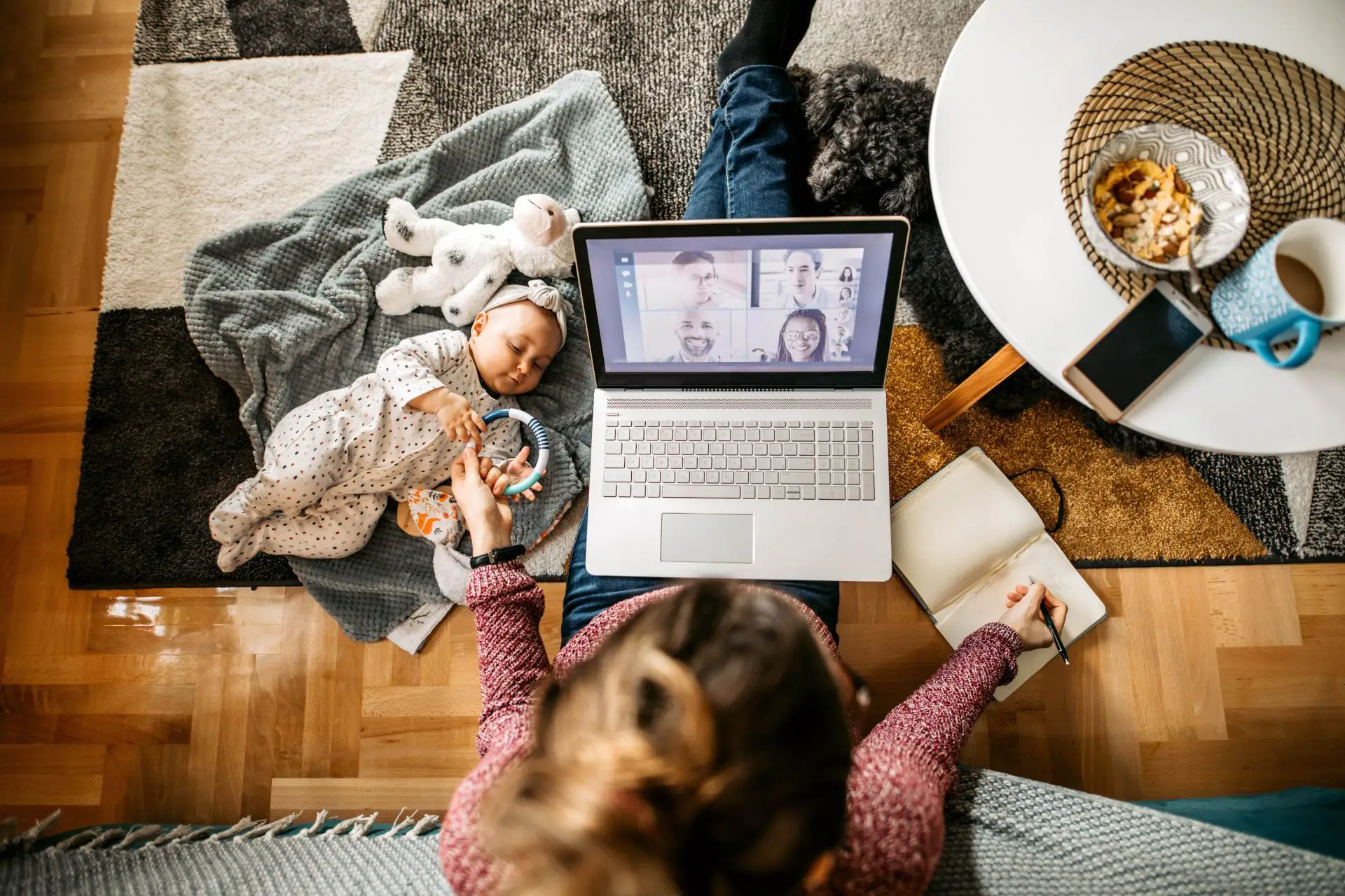 A woman working on her laptop with a child next to her, trying to eat some lunch