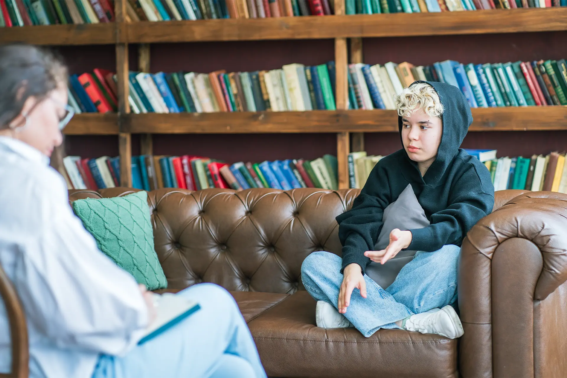 A young person on a couch looking unhappy and talking to an adult, possibly a therapist