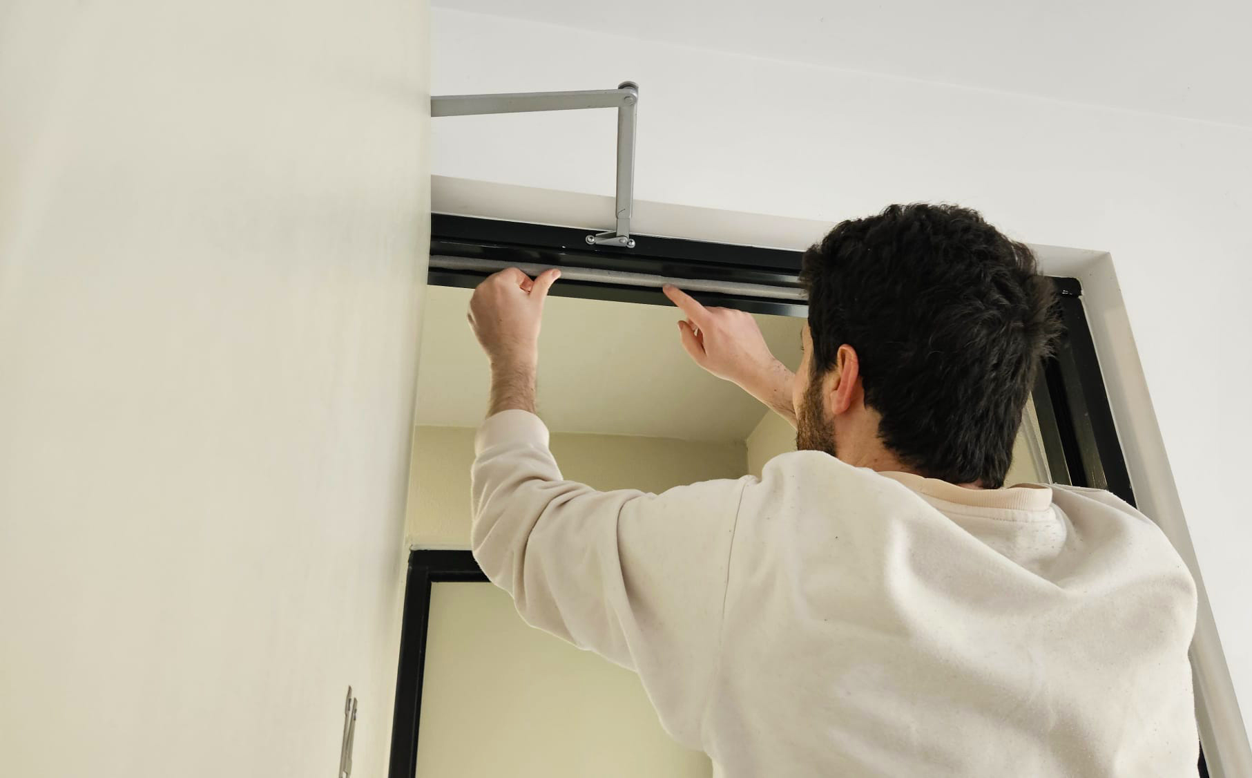 A younger man installing weather stripping on a door frame