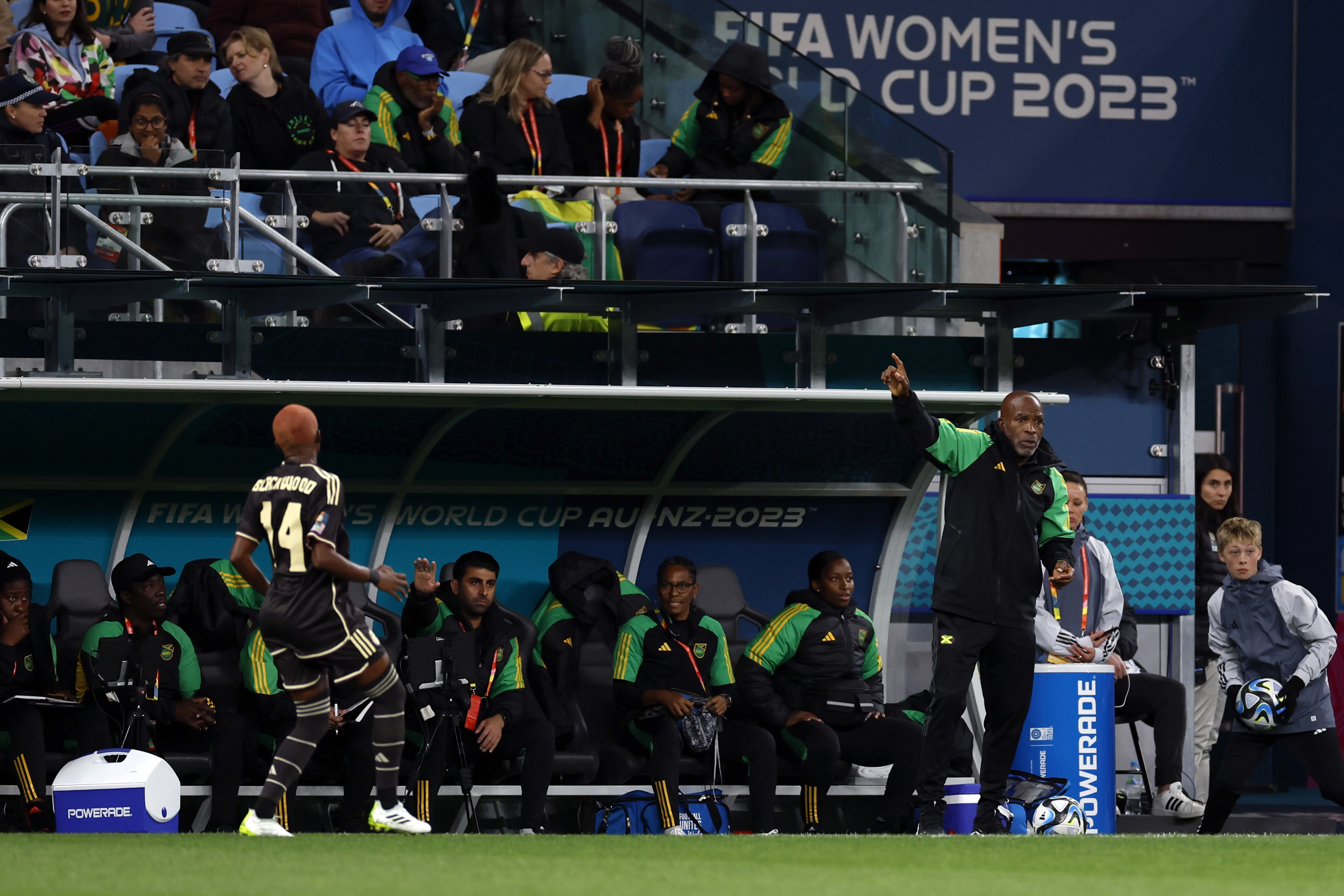 Head Coach of the Jamaican women’s soccer team points to players from the bench with other coaches offering advice
