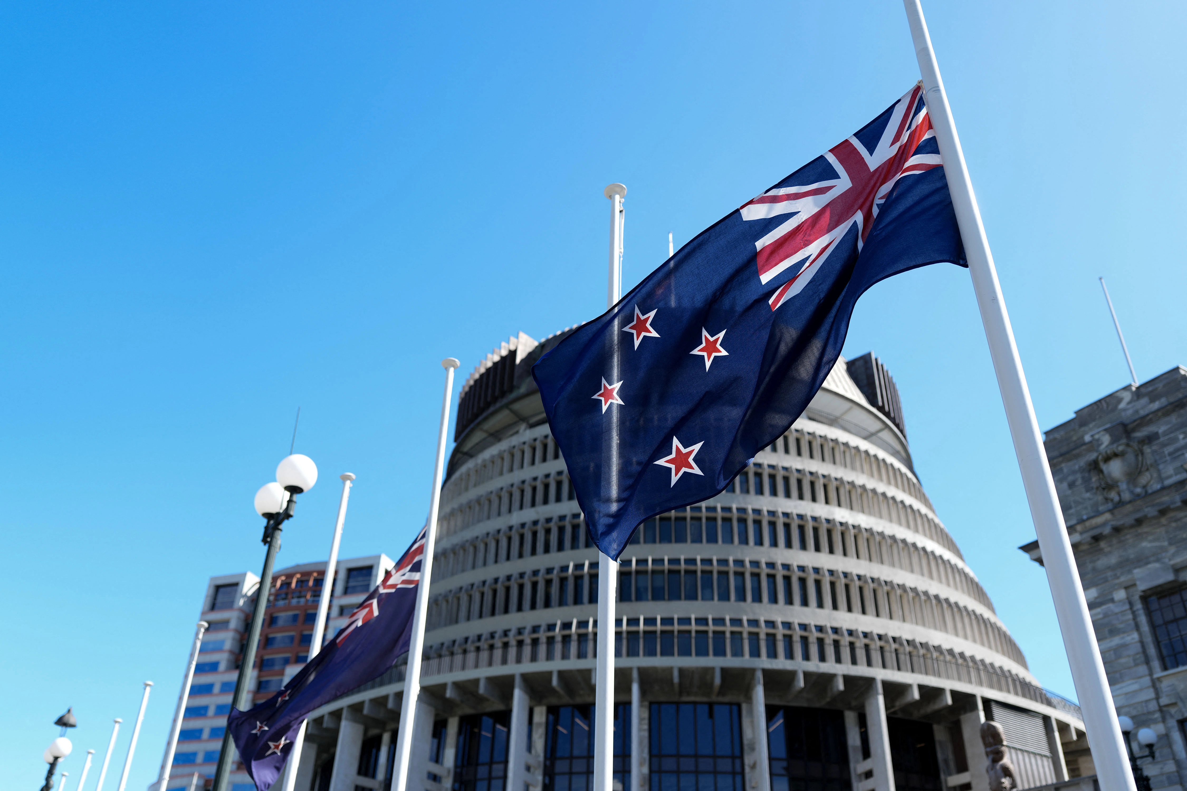 Two New Zealand flags flapping in the wind on a flagpole in front of a government building