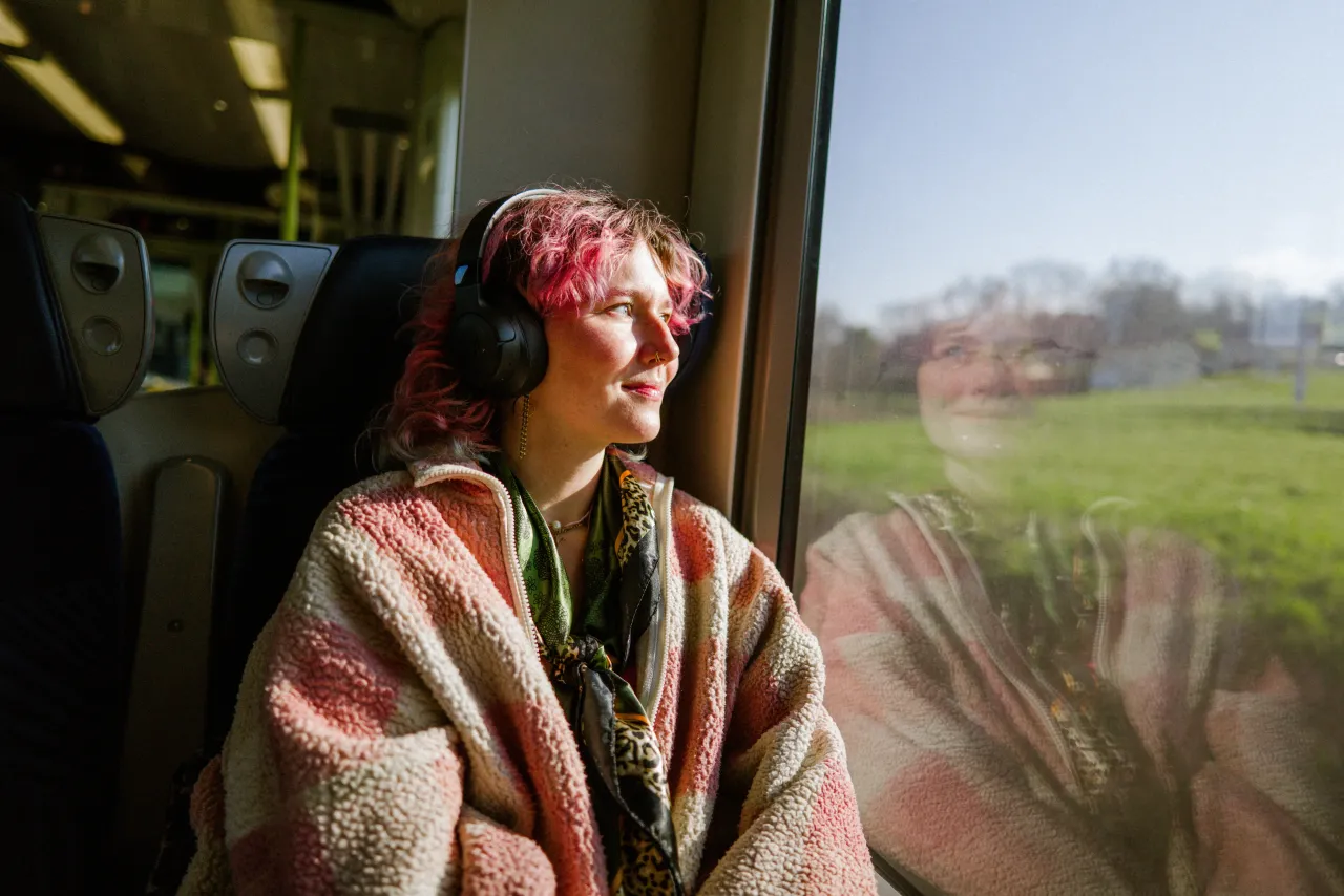 A woman looks out the window of a train with headphones on