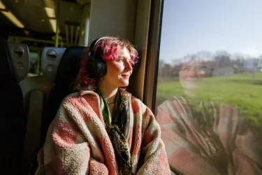 A woman looks out the window of a train with headphones on